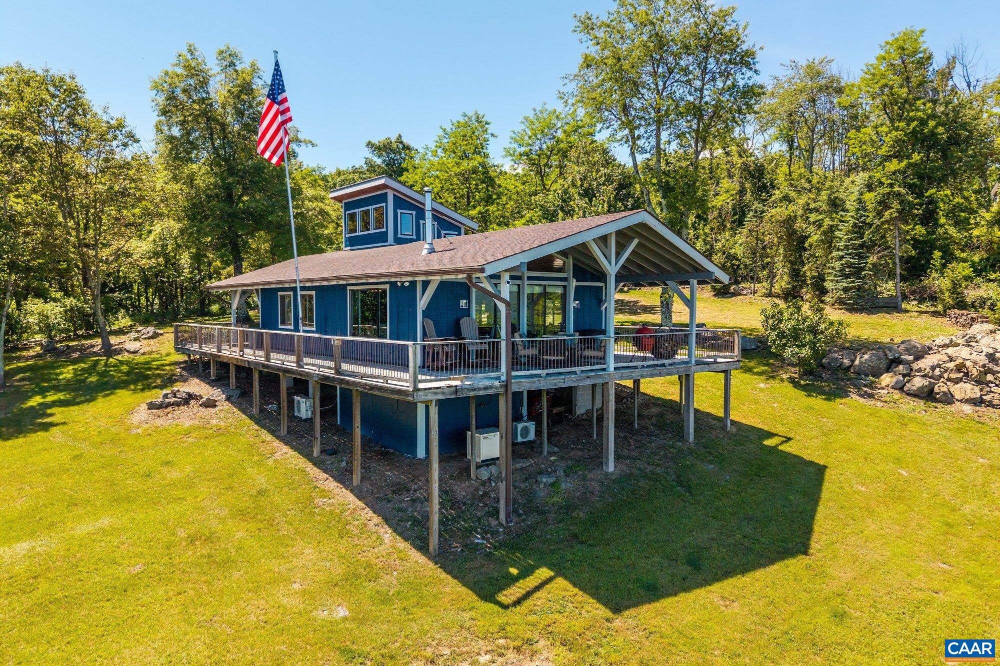 Set high in the rolling hills of Flattop Mountain, this rare mountain cabin offers 3 acres of private land and some of the most striking views in Virginia. Perched near Free Union, the property boasts sweeping vistas of the Blue Ridge Mountains and the valley below. Designed with an open-concept layout, the interior can comfortably sleep up to 10 depending on configuration, with living, dining, and kitchen areas all sharing one bright, rustic space filled with natural light. A 950-square-foot covered wraparound porch offers panoramic views and the perfect setting for relaxing, entertaining, or enjoying a barbecue in any weather. Unlike many mountain homes, this one offers the unique advantage of a view that’s easy to maintain, with direct access to a service road that makes upkeep straightforward year-round. A private well delivers some of the best-tasting water on the mountain, and the location benefits from quick snowmelt in winter thanks to its ideal position on the slope. An in-ground propane tank and generator ensure comfort and reliability year-round. Community amenities include a pool, tennis court, and access to the Appalachian Trail via an HOA-owned lot, adding to the property’s appeal as a gateway to outdoor recreation.