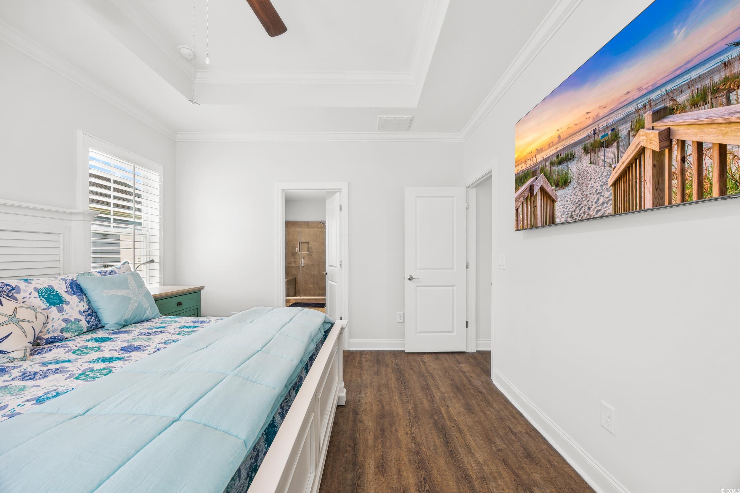 Bedroom featuring ceiling fan, a raised ceiling, dark hardwood / wood-style flooring, ensuite bathroom, and crown molding