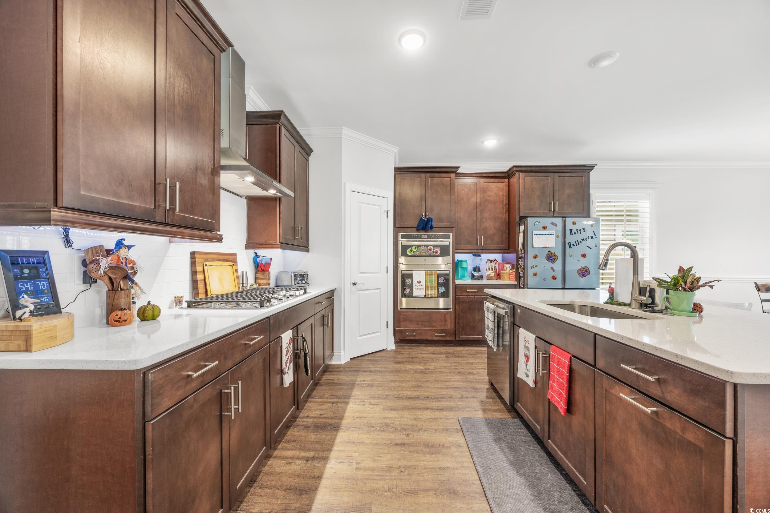 Kitchen featuring wall chimney range hood, appliances with stainless steel finishes, ornamental molding, light hardwood / wood-style floors, and sink