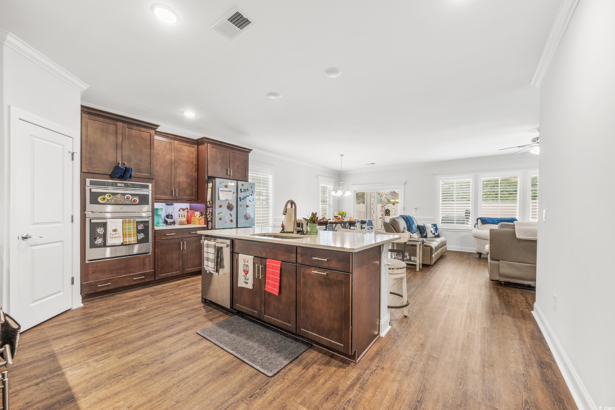 Kitchen featuring stainless steel appliances, wood-type flooring, a center island with sink, sink, and crown molding