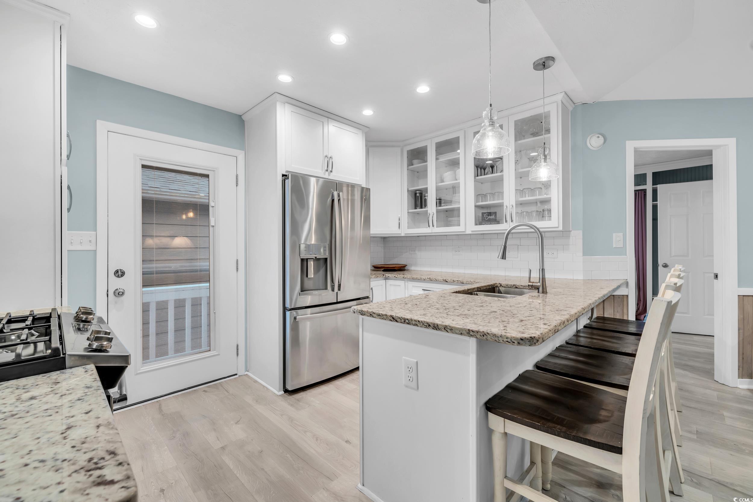 Kitchen featuring sink, pendant lighting, stainless steel fridge, and light stone counters