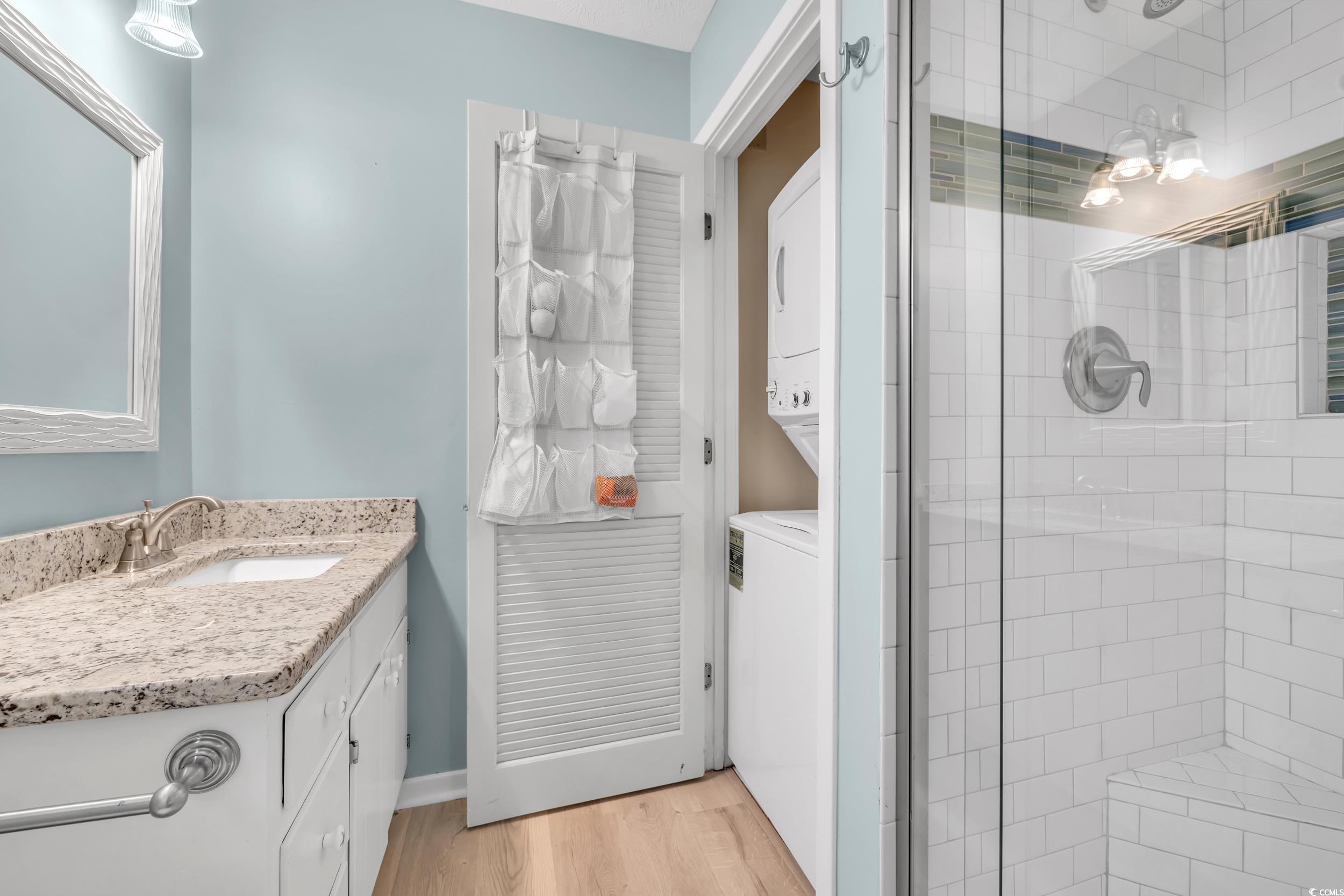 Bathroom with hardwood / wood-style flooring, vanity, stacked washer / drying machine, and walk in shower