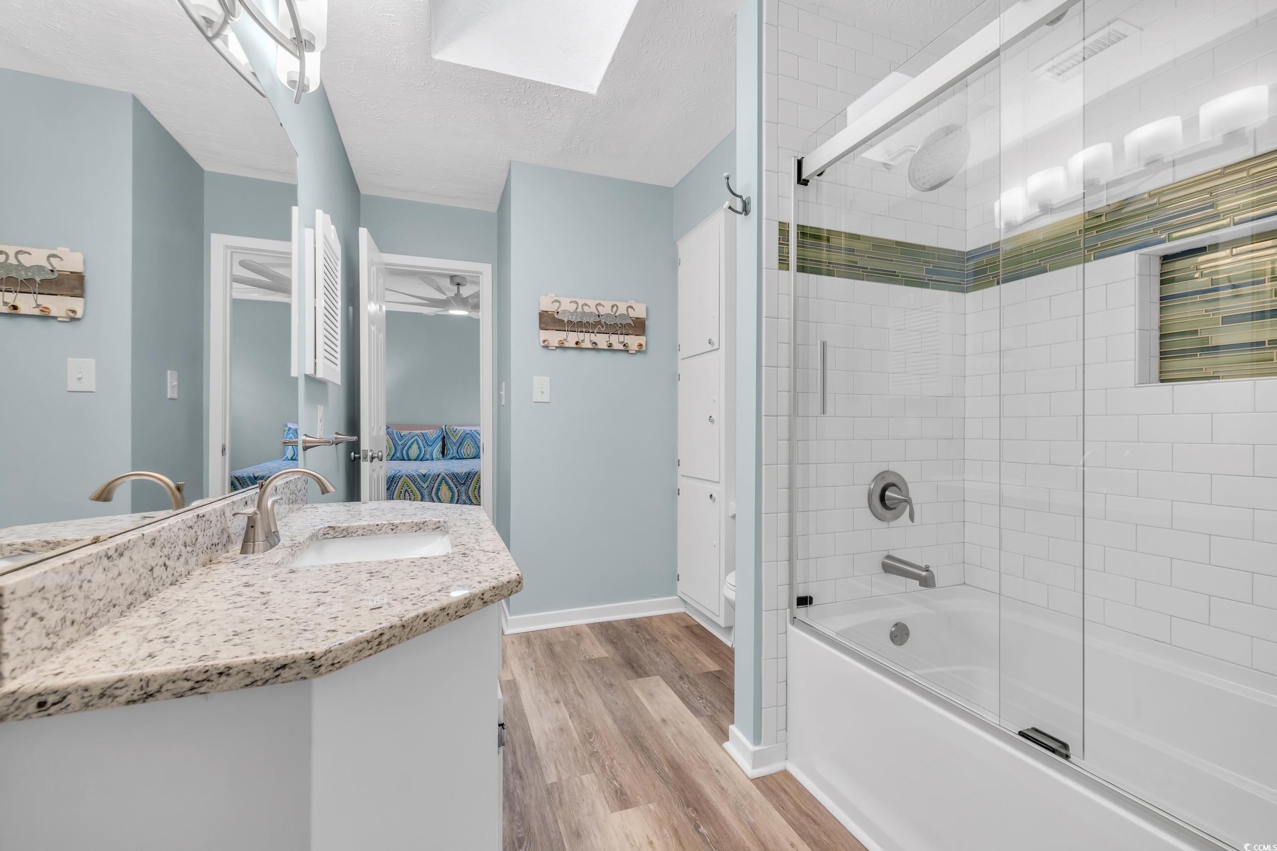 Full bathroom with enclosed tub / shower combo, vanity, wood-type flooring, a textured ceiling, and toilet