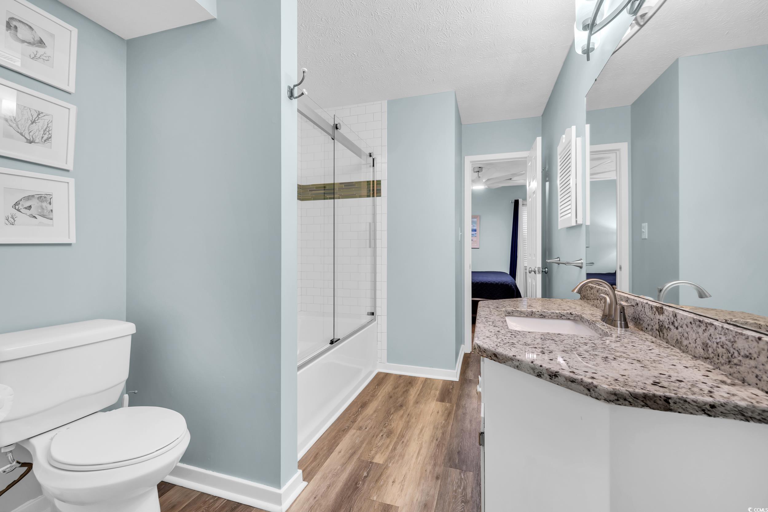 Full bathroom featuring hardwood / wood-style flooring, bath / shower combo with glass door, vanity, a textured ceiling, and toilet