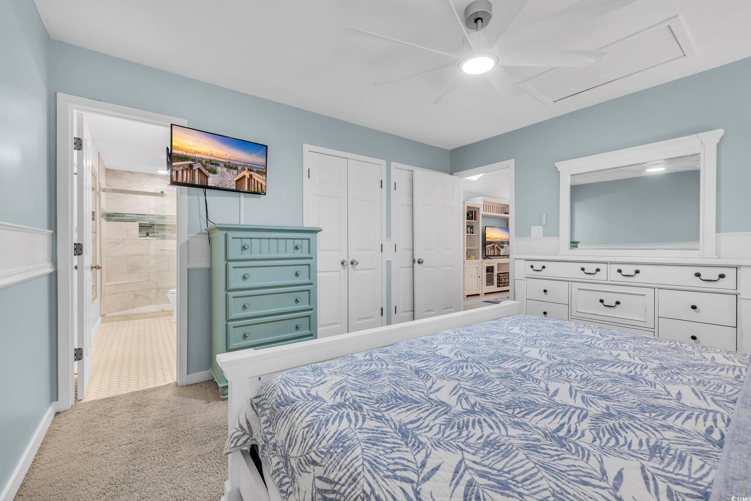 Bedroom with connected bathroom, light colored carpet, and ceiling fan