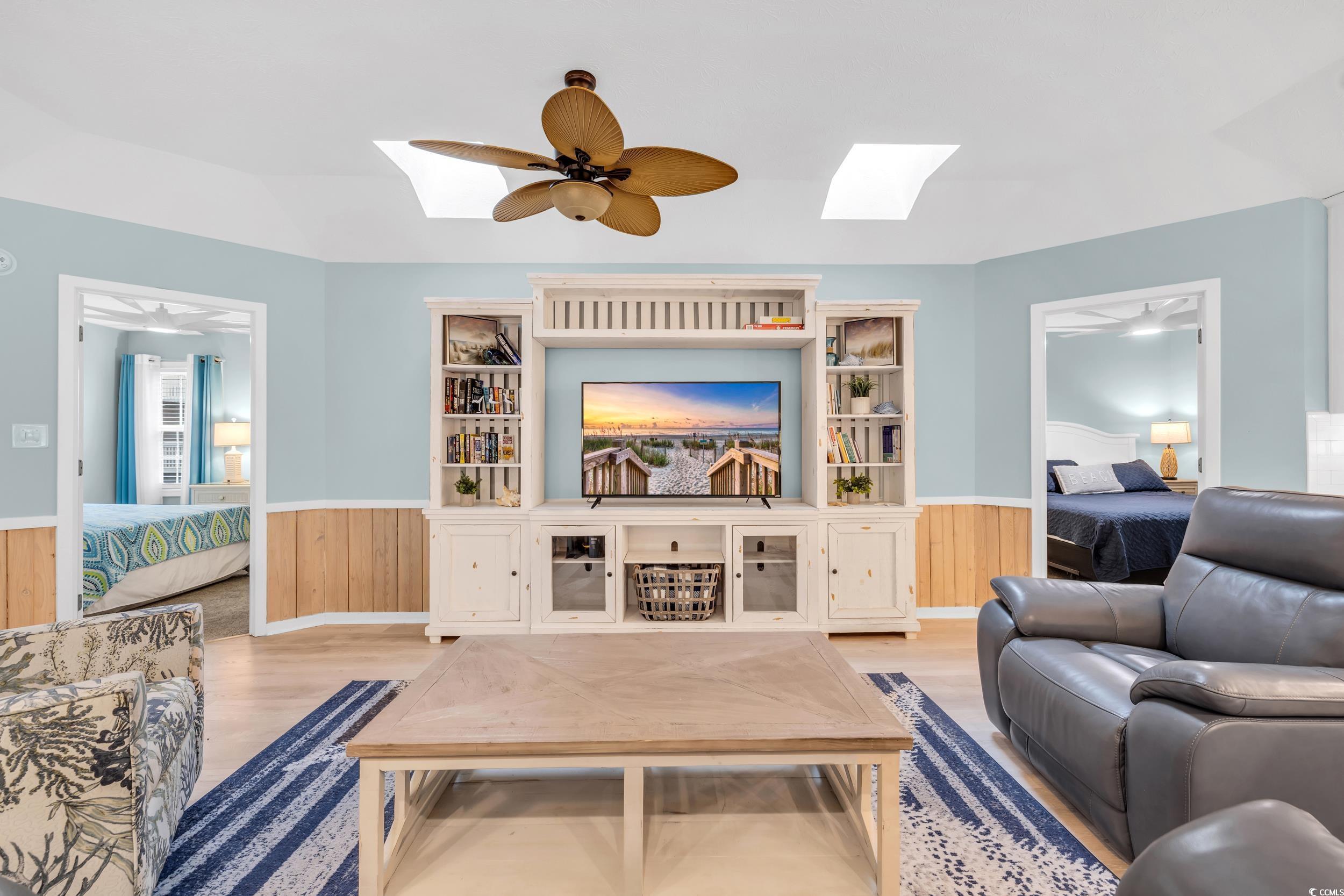 Living room featuring a skylight, wooden walls, ceiling fan, and light wood-type flooring