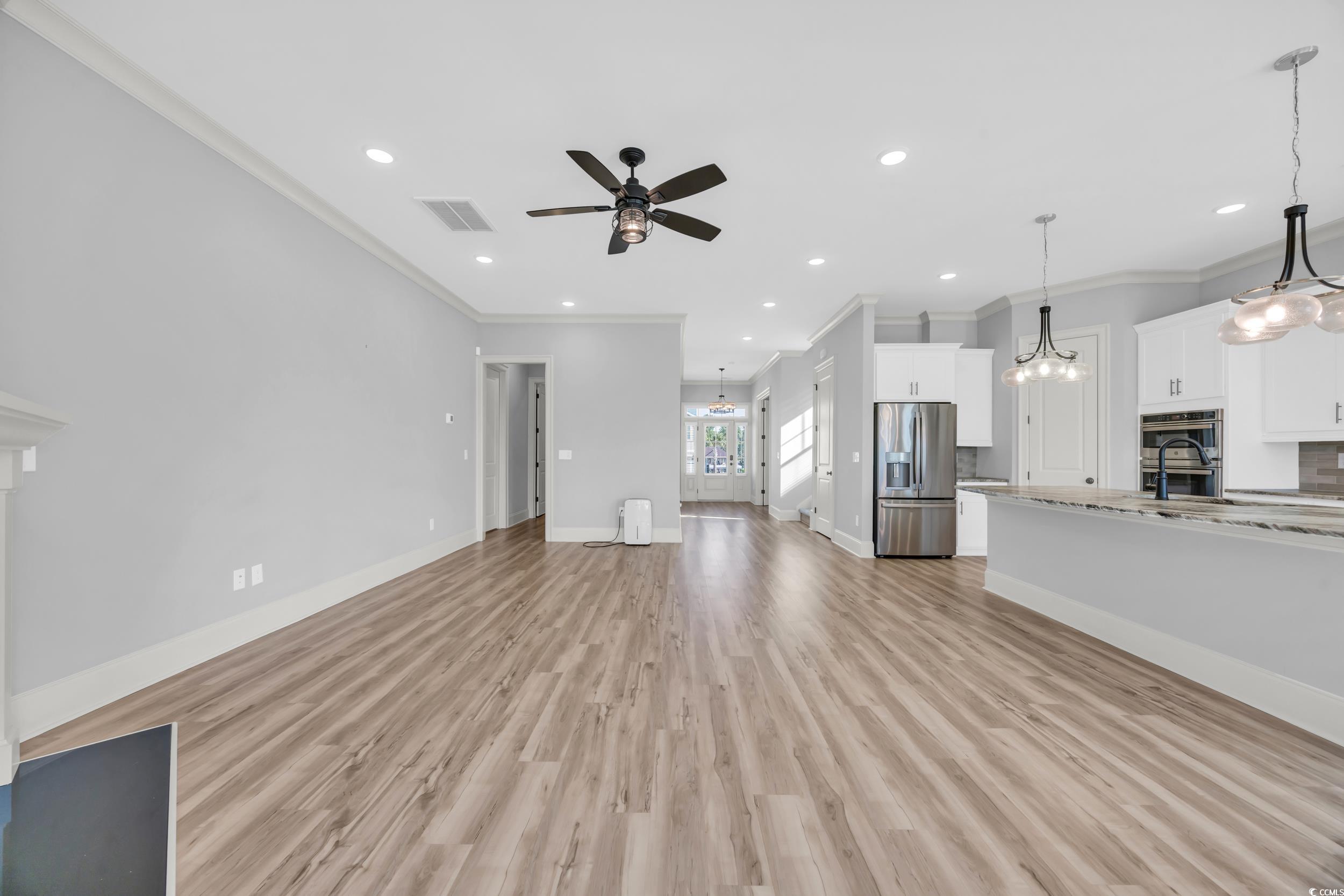 Unfurnished living room featuring ornamental molding, ceiling fan, light wood-type flooring, a chandelier, and baseboards