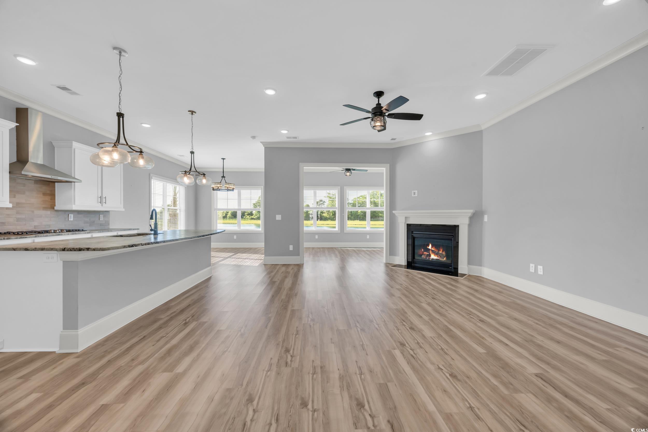 Unfurnished living room featuring crown molding, a ceiling fan, light wood-type flooring, a fireplace with flush hearth, and recessed lighting