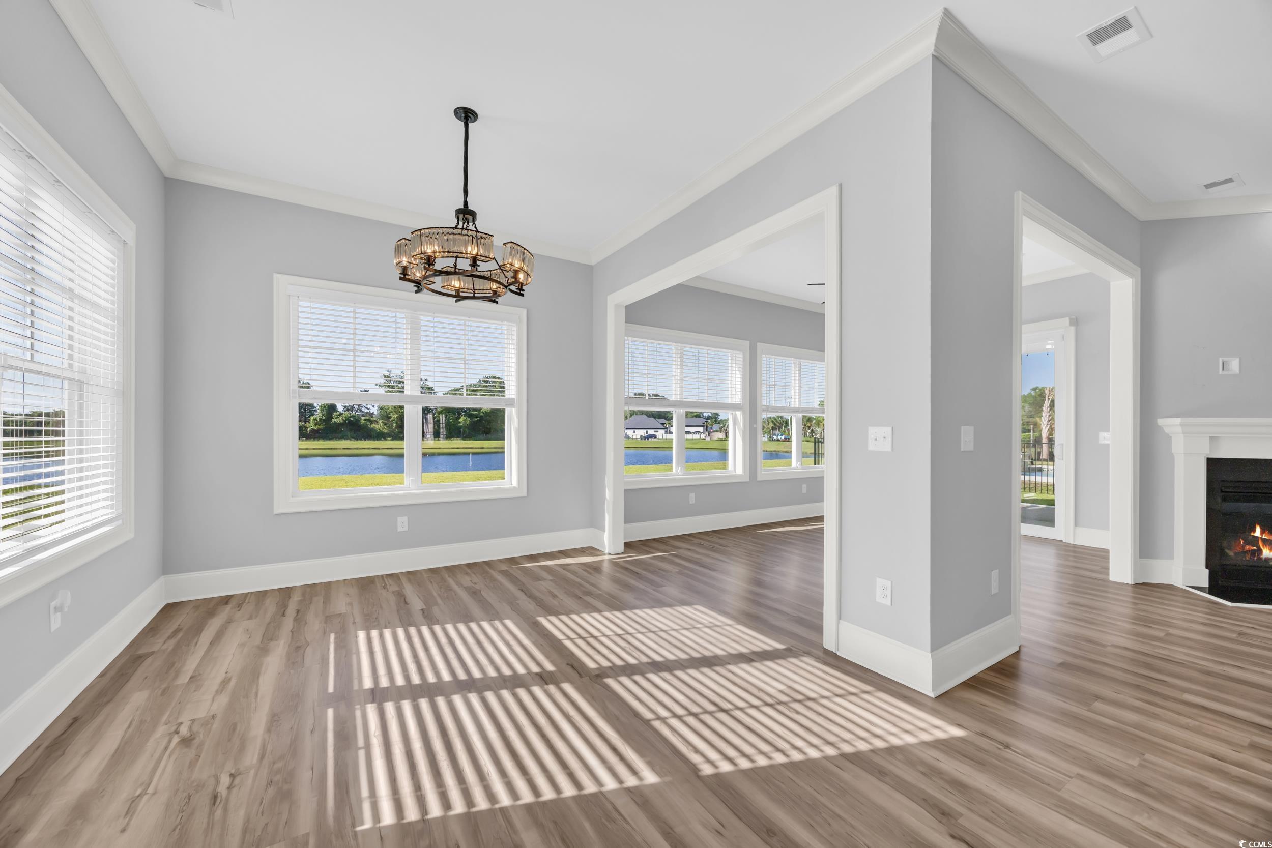 Unfurnished dining area with crown molding, wood finished floors, a fireplace with flush hearth, a chandelier, and baseboards