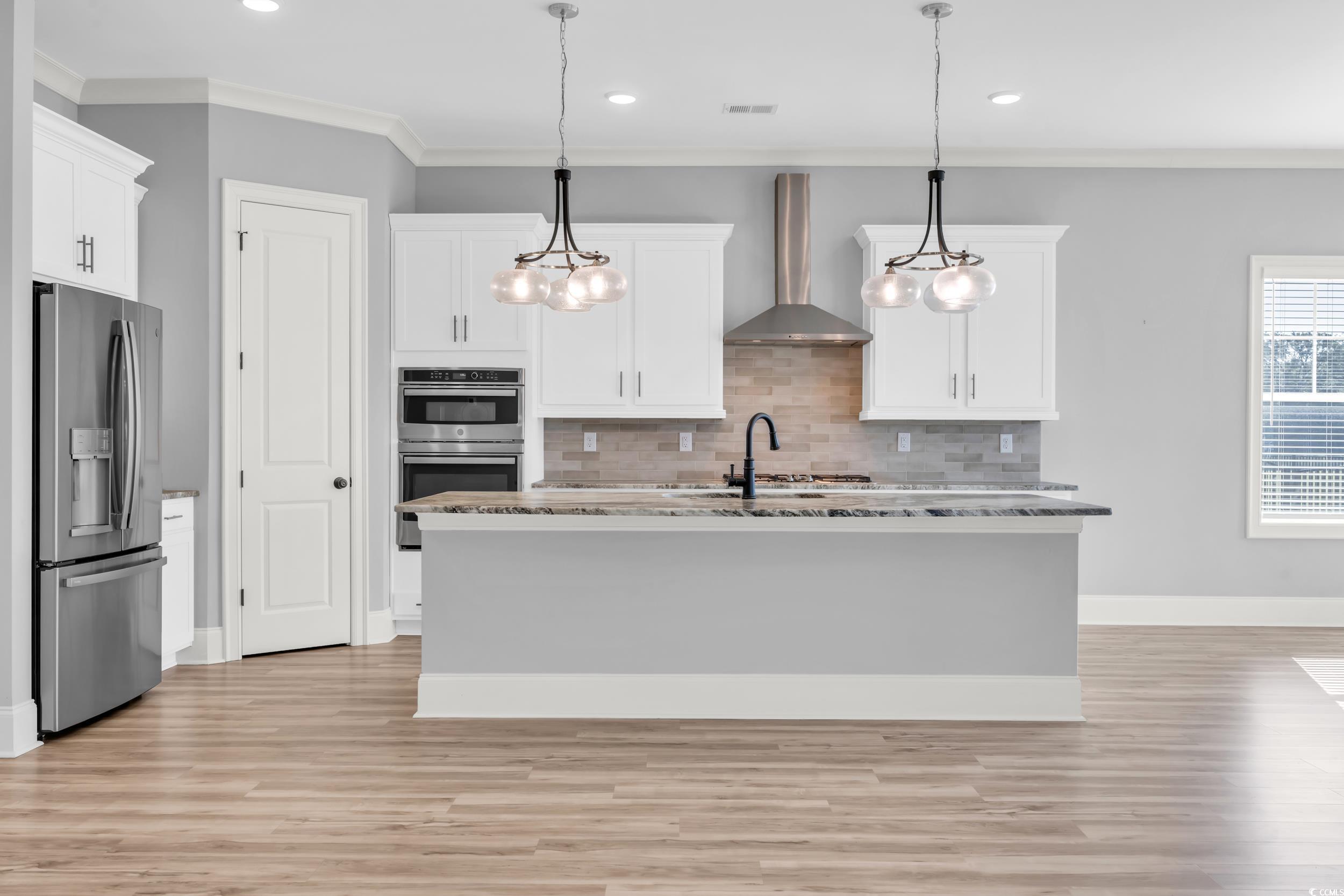 Kitchen with stainless steel appliances, wall chimney range hood, backsplash, white cabinetry, and recessed lighting