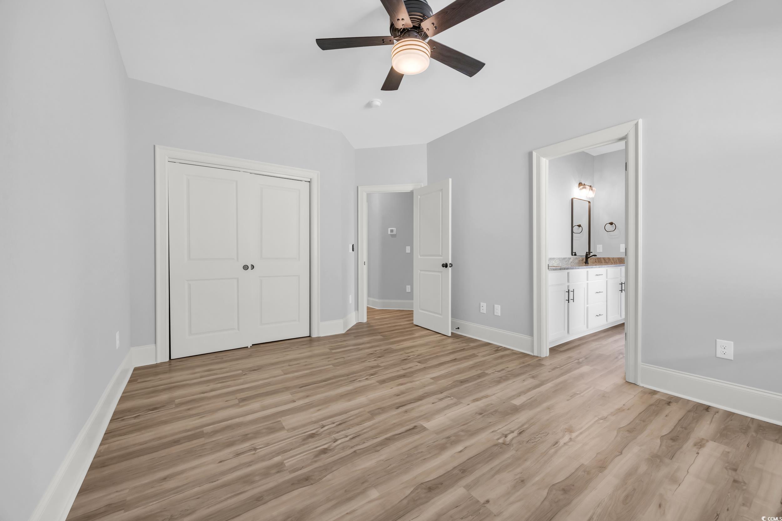 Unfurnished bedroom with light wood finished floors, baseboards, a closet, ensuite bath, and a ceiling fan