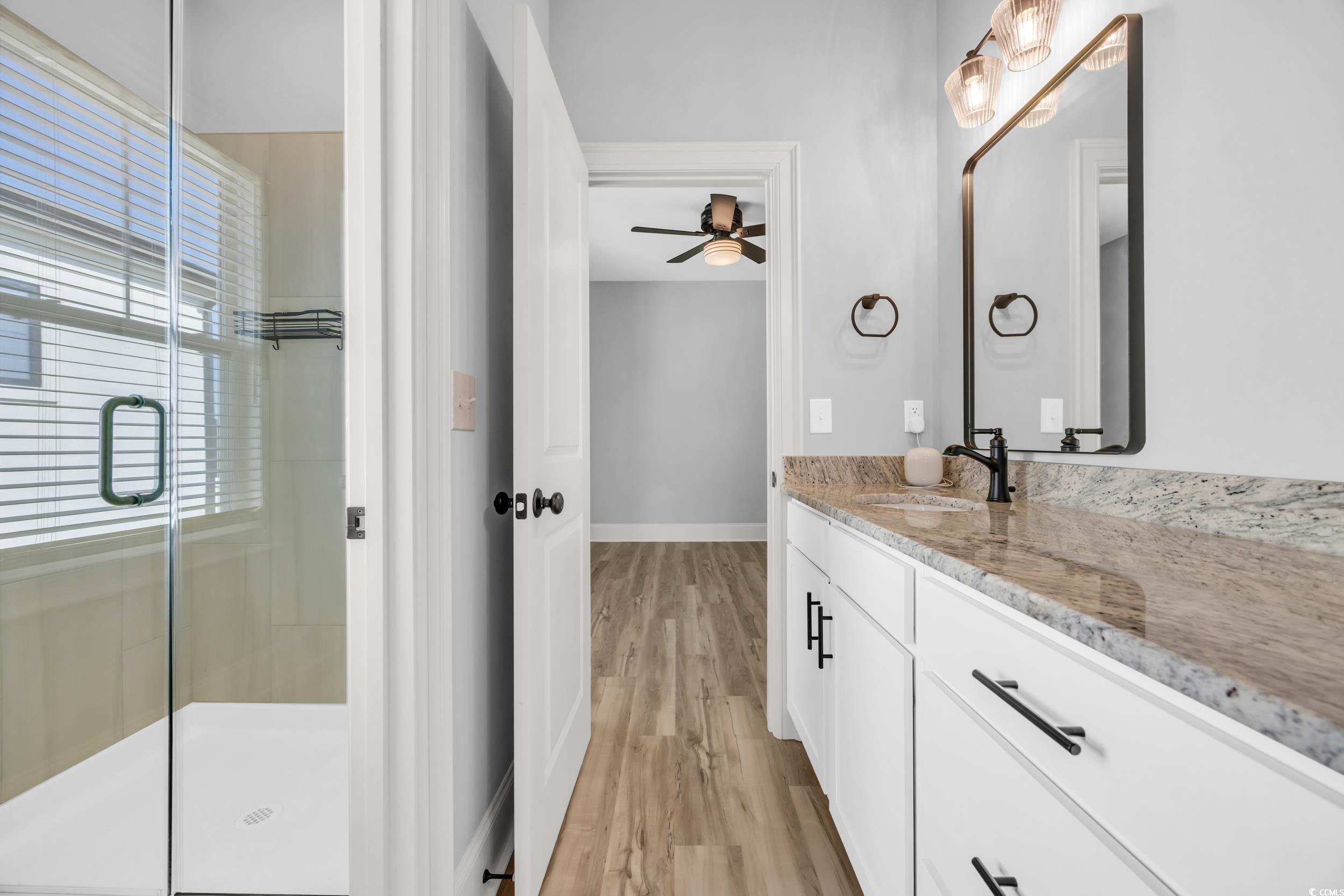 Full bathroom with a shower stall, wood finished floors, baseboards, vanity, and ceiling fan