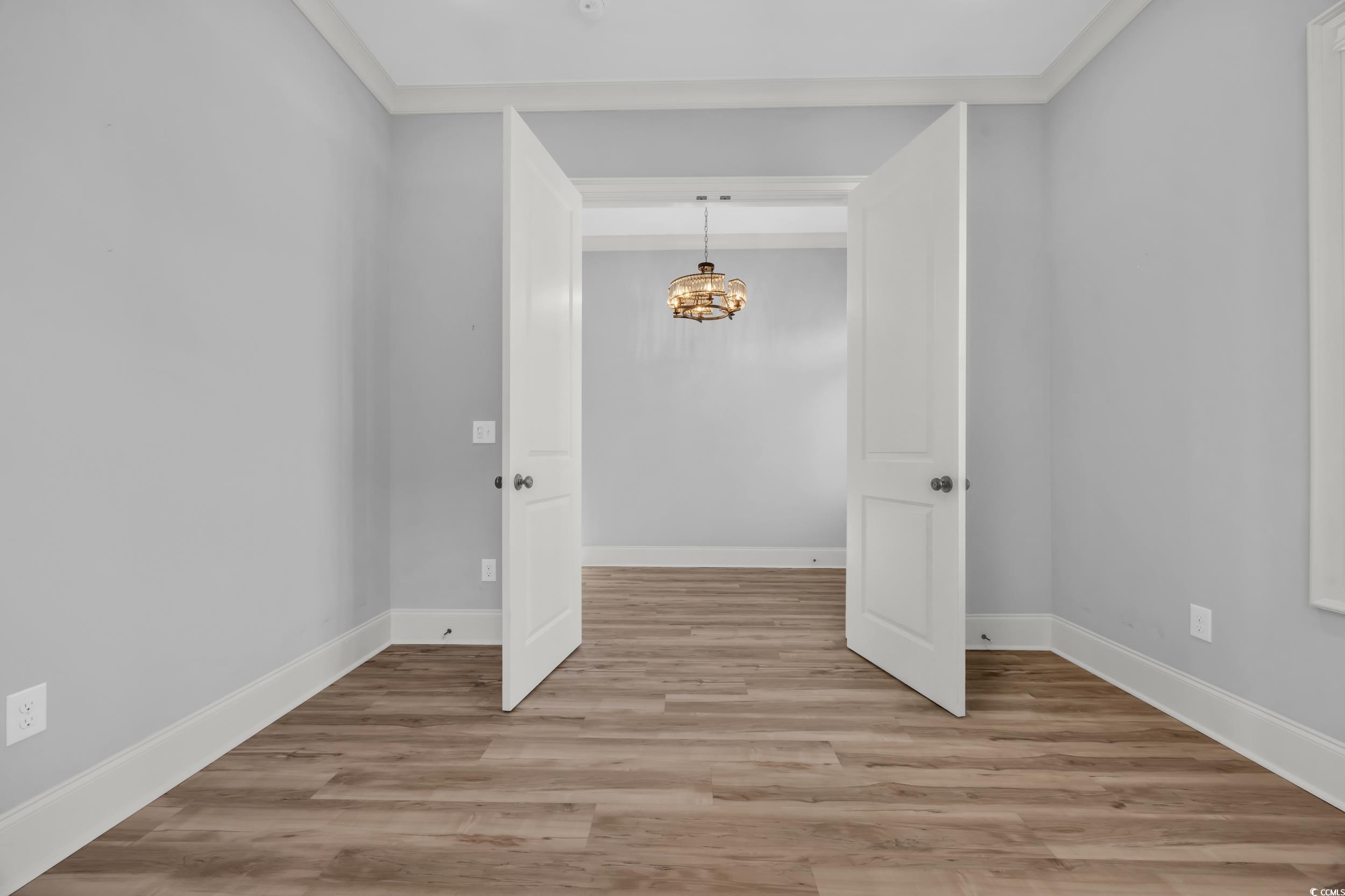 Empty room with a chandelier, light wood-style floors, and baseboards