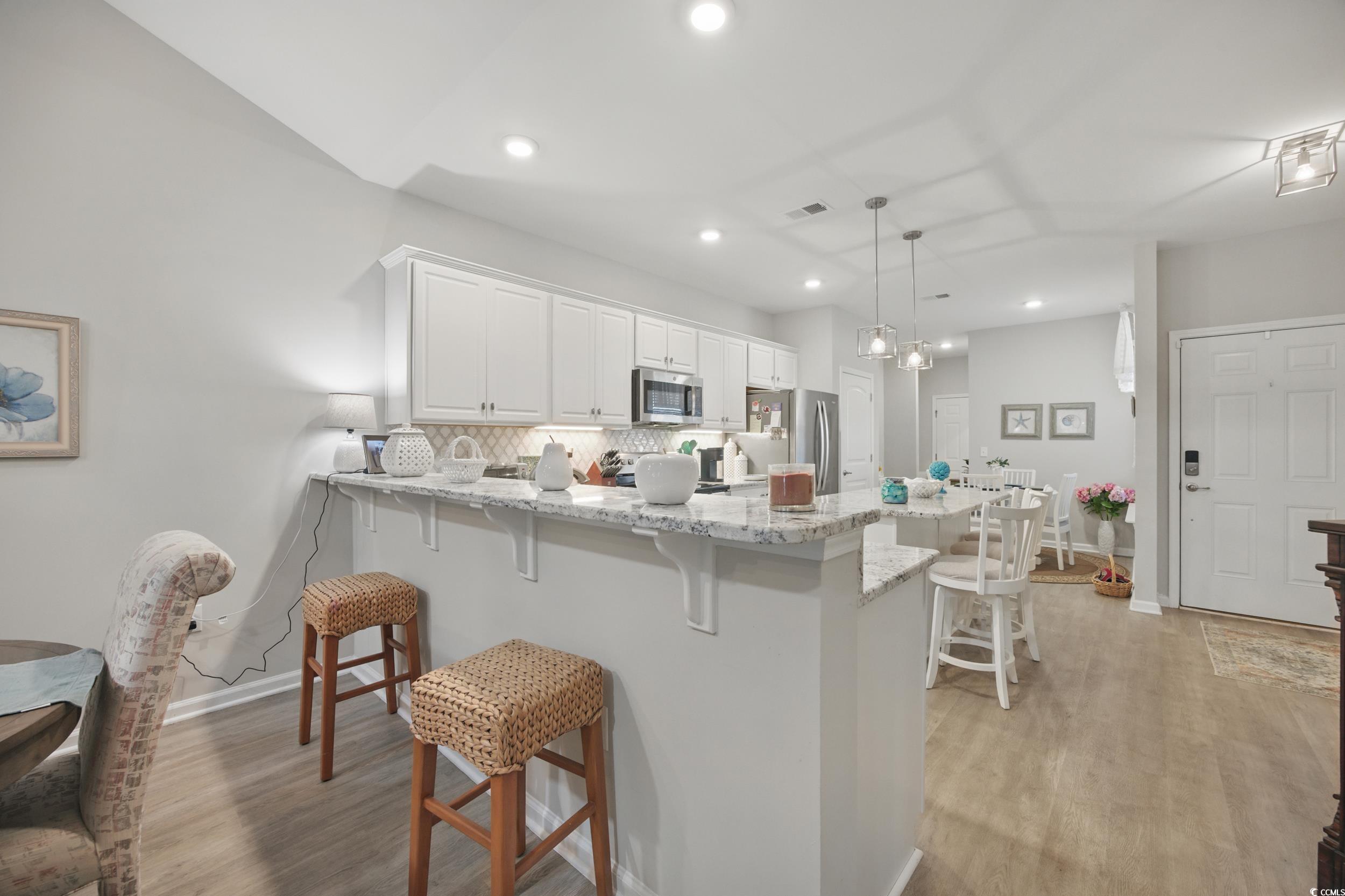 Kitchen featuring stainless steel appliances, a kitchen breakfast bar, a peninsula, baseboards, and white cabinets