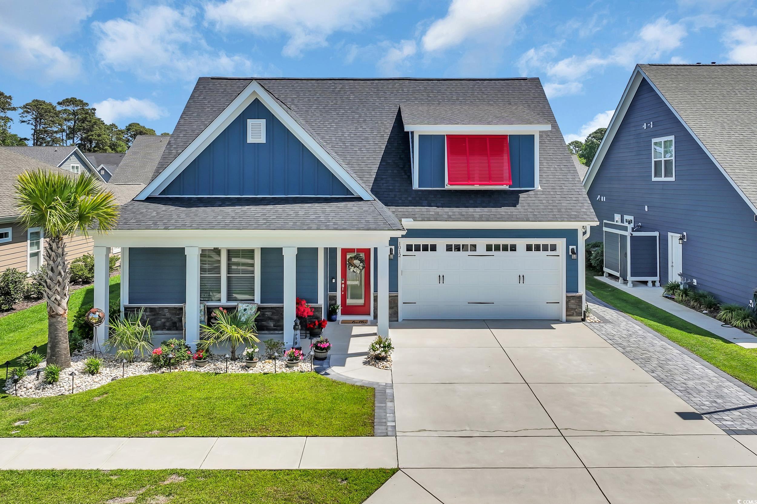 View of front of home with board and batten siding, a porch, driveway, a shingled roof, and a front yard