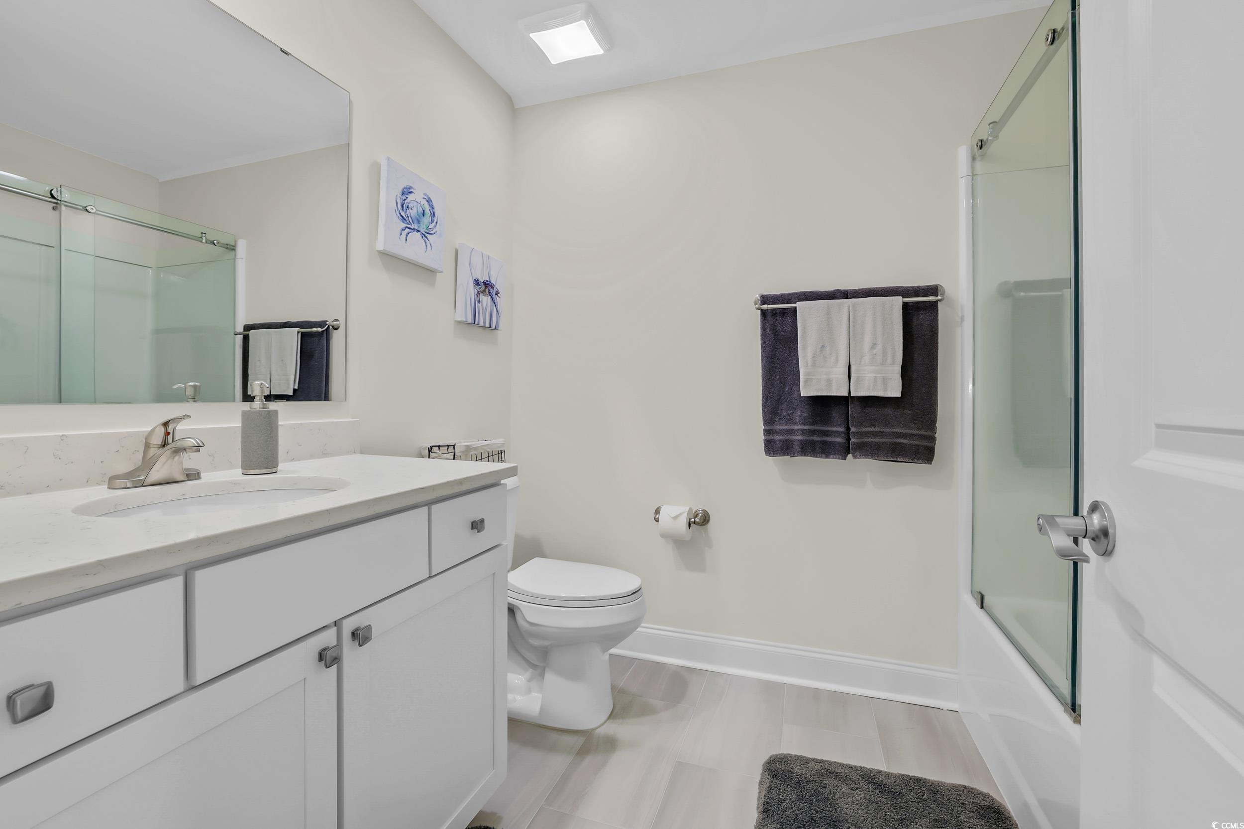 Full bath featuring toilet, vanity, baseboards, and enclosed tub / shower combo
