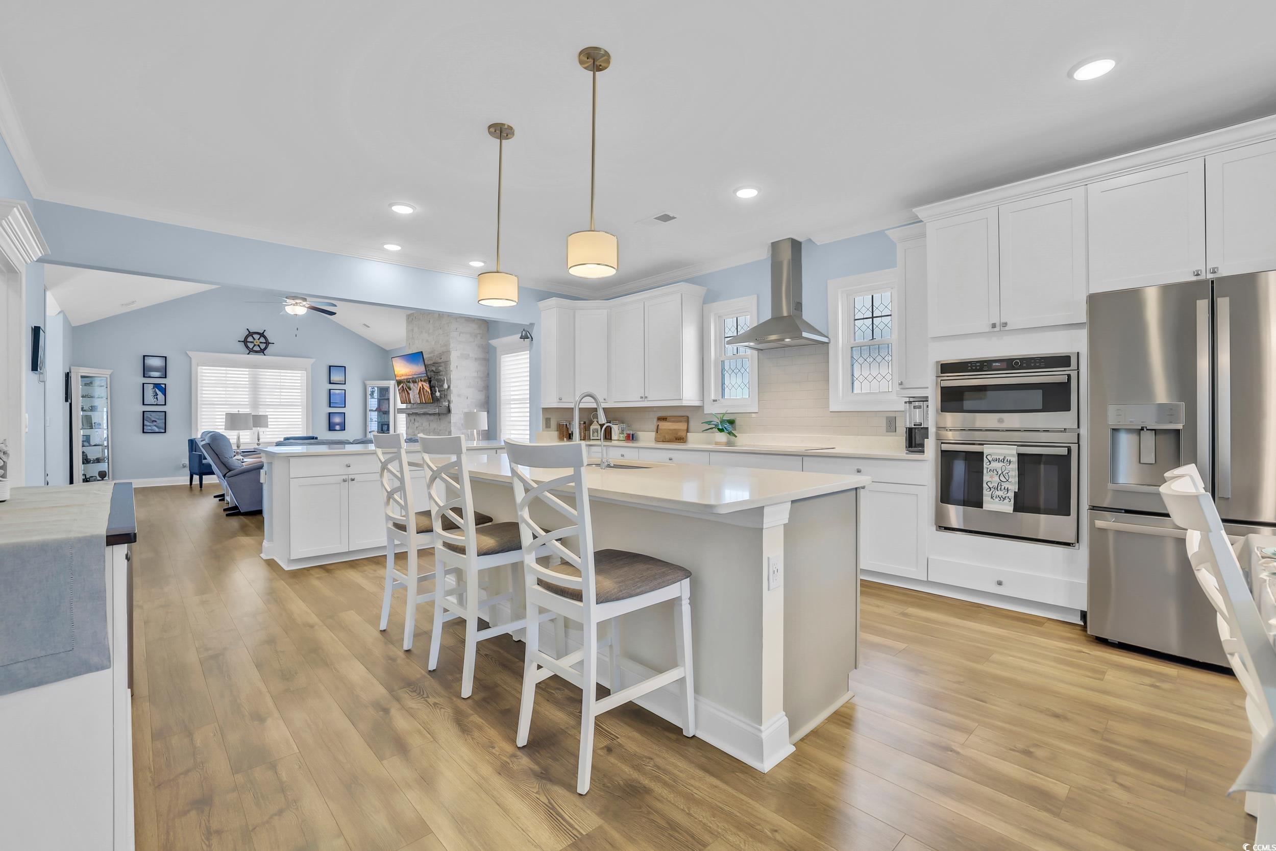 Kitchen featuring stainless steel appliances, wall chimney exhaust hood, open floor plan, light countertops, and white cabinetry