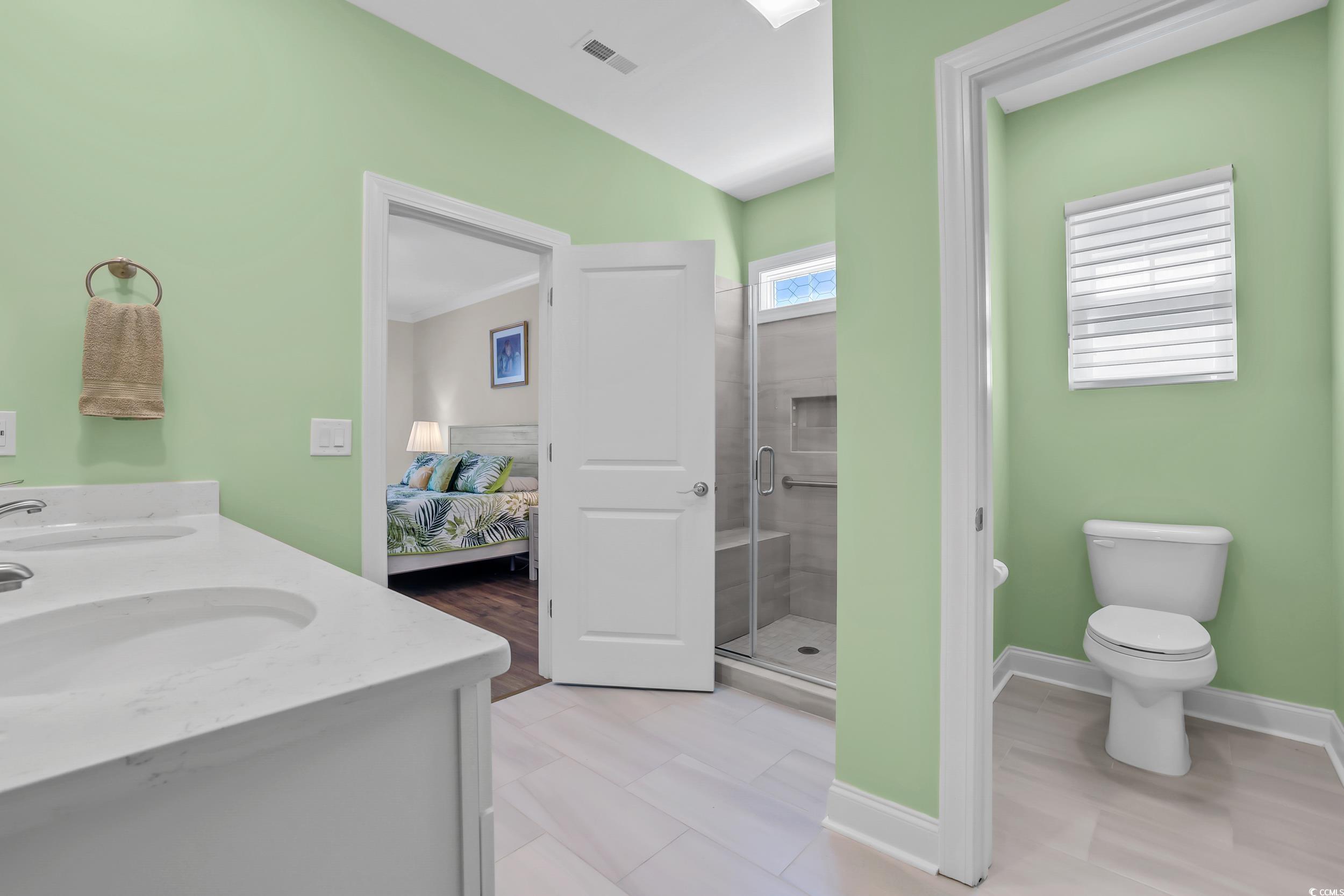 Full bathroom featuring ensuite bath, a stall shower, toilet, double vanity, and vaulted ceiling