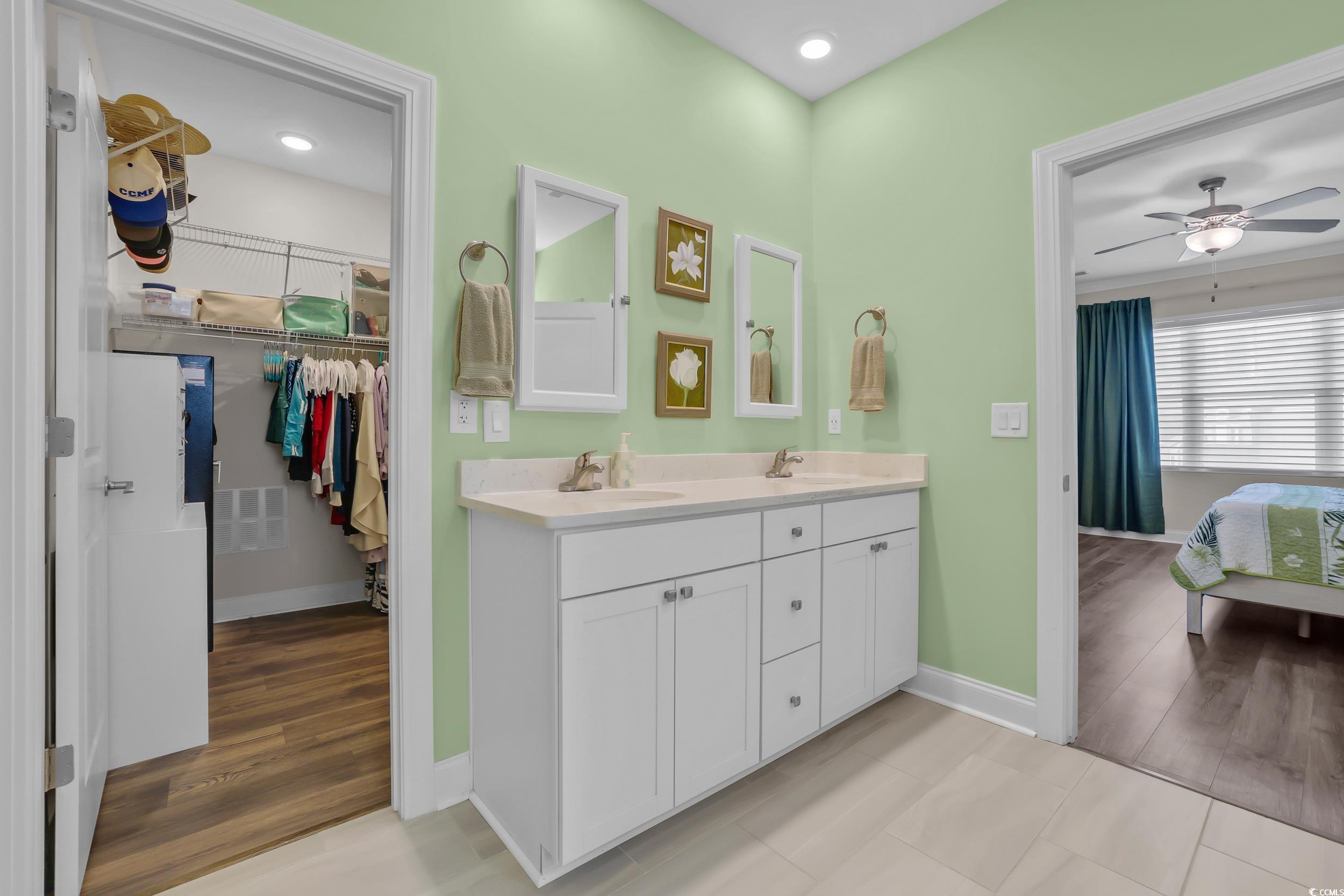 Full bath with baseboards, a ceiling fan, double vanity, a spacious closet, and ensuite bathroom