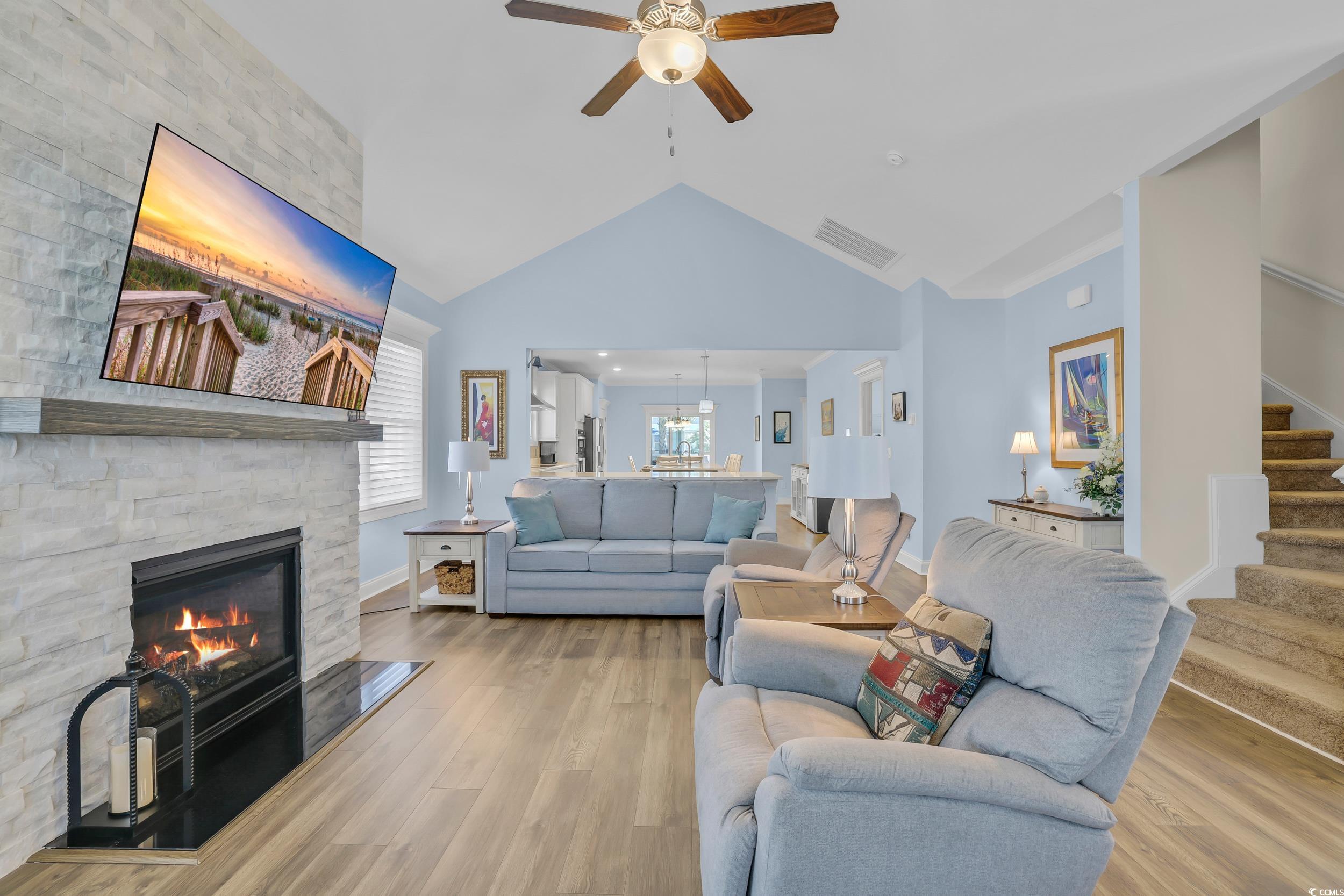 Living area with ceiling fan, stairway, vaulted ceiling, a fireplace, and light wood-style flooring