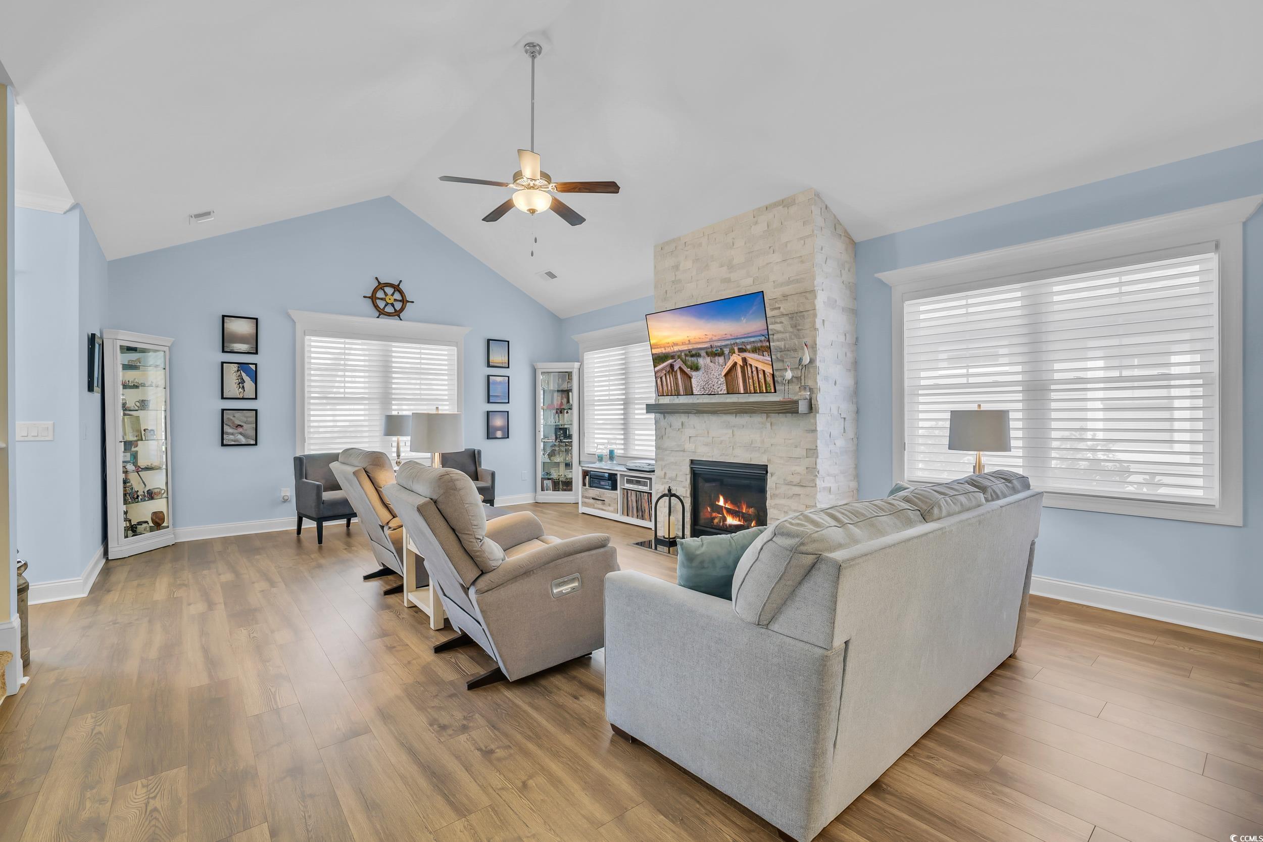 Living area with ceiling fan, a fireplace, wood finished floors, baseboards, and high vaulted ceiling