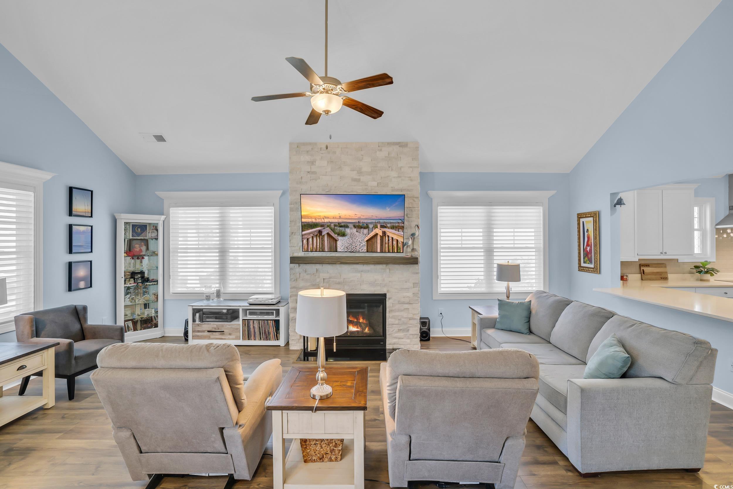 Living room featuring ceiling fan, a stone fireplace, wood finished floors, and high vaulted ceiling