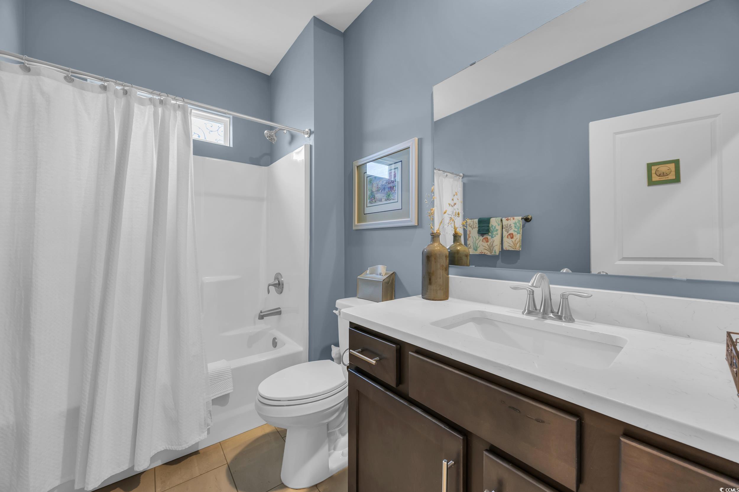 Full bath featuring vanity, toilet, shower / bath combo with shower curtain, and tile patterned flooring