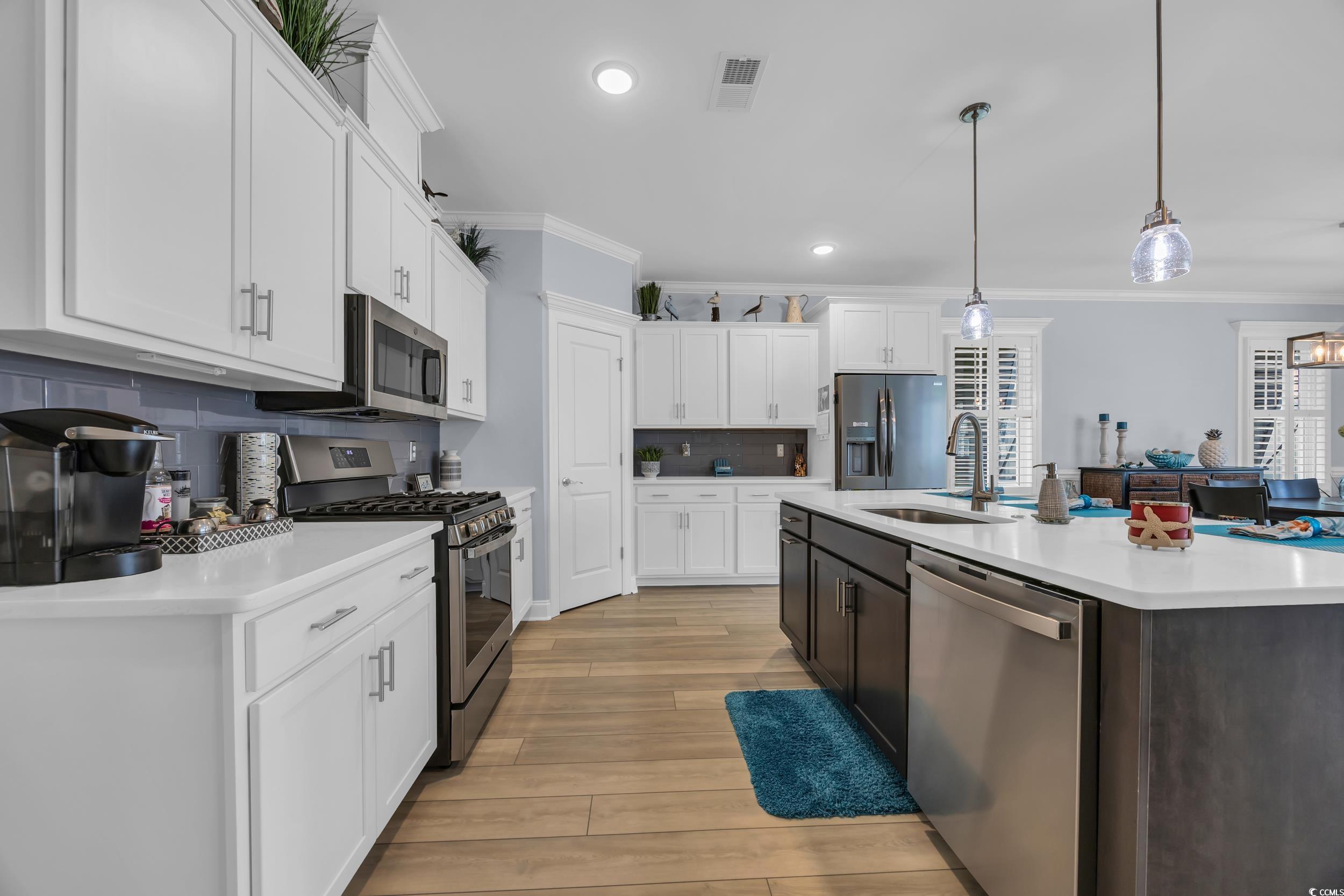 Kitchen with appliances with stainless steel finishes, crown molding, light countertops, a sink, and white cabinets