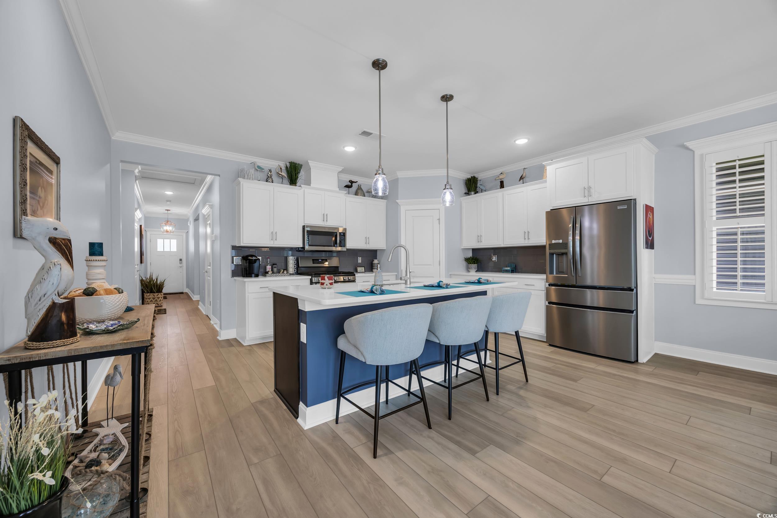 Kitchen with stainless steel appliances, tasteful backsplash, a breakfast bar, white cabinetry, and ornamental molding
