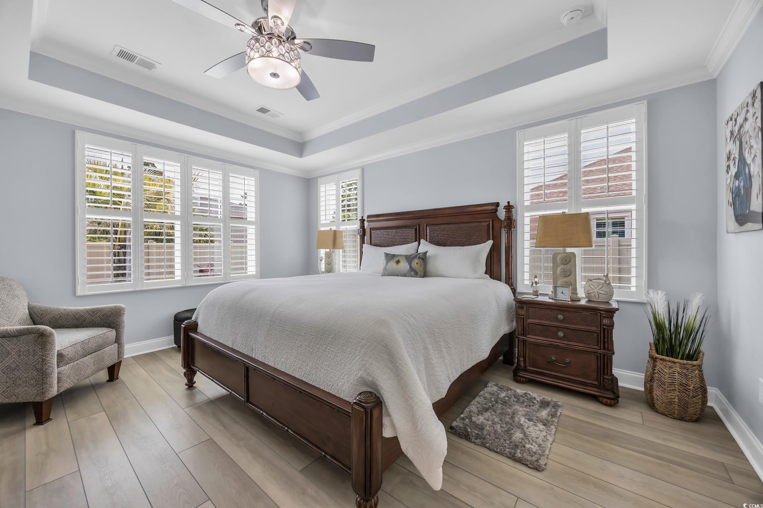 Bedroom featuring a tray ceiling, crown molding, light wood finished floors, and baseboards
