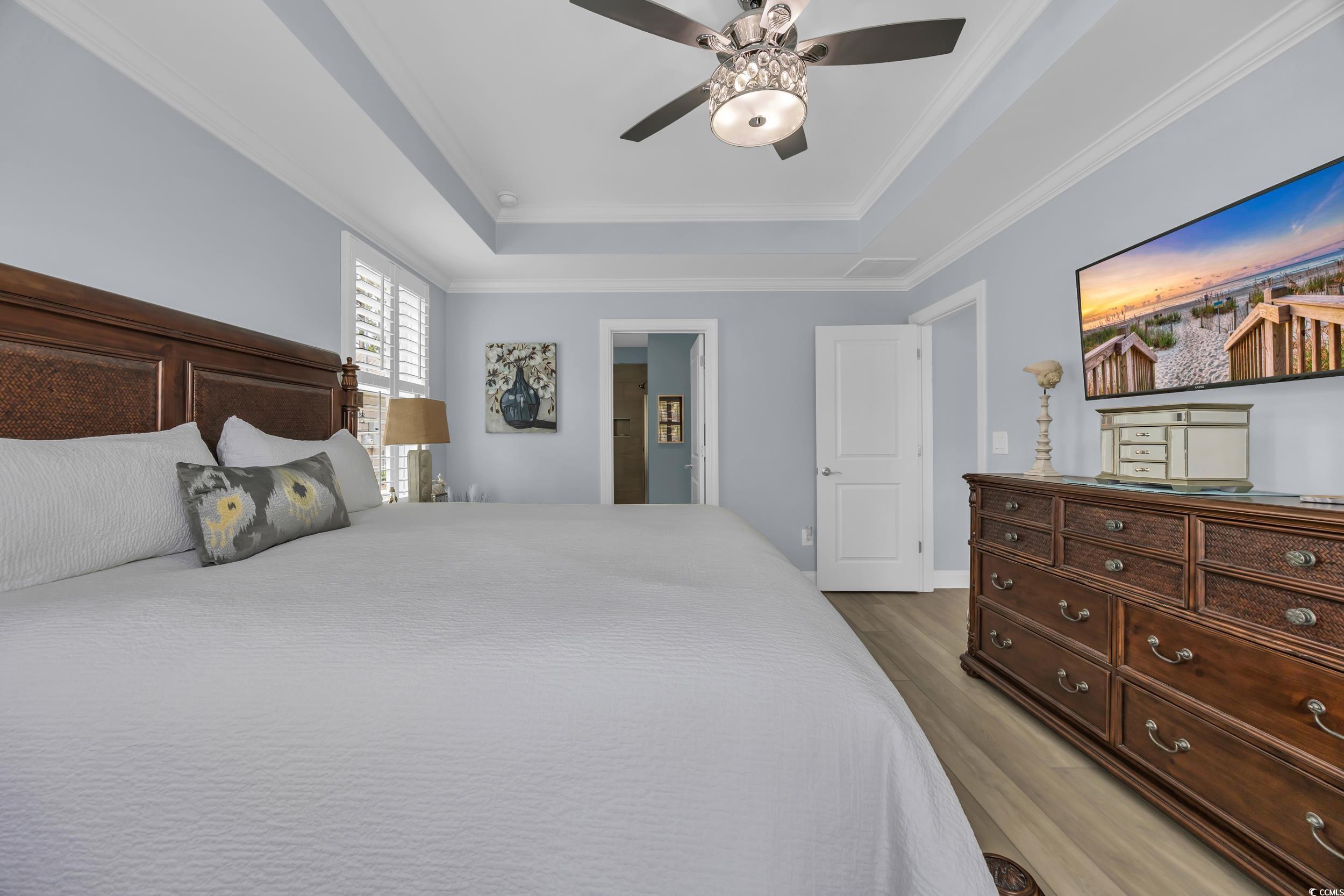 Bedroom with a tray ceiling, wood finished floors, crown molding, and a ceiling fan