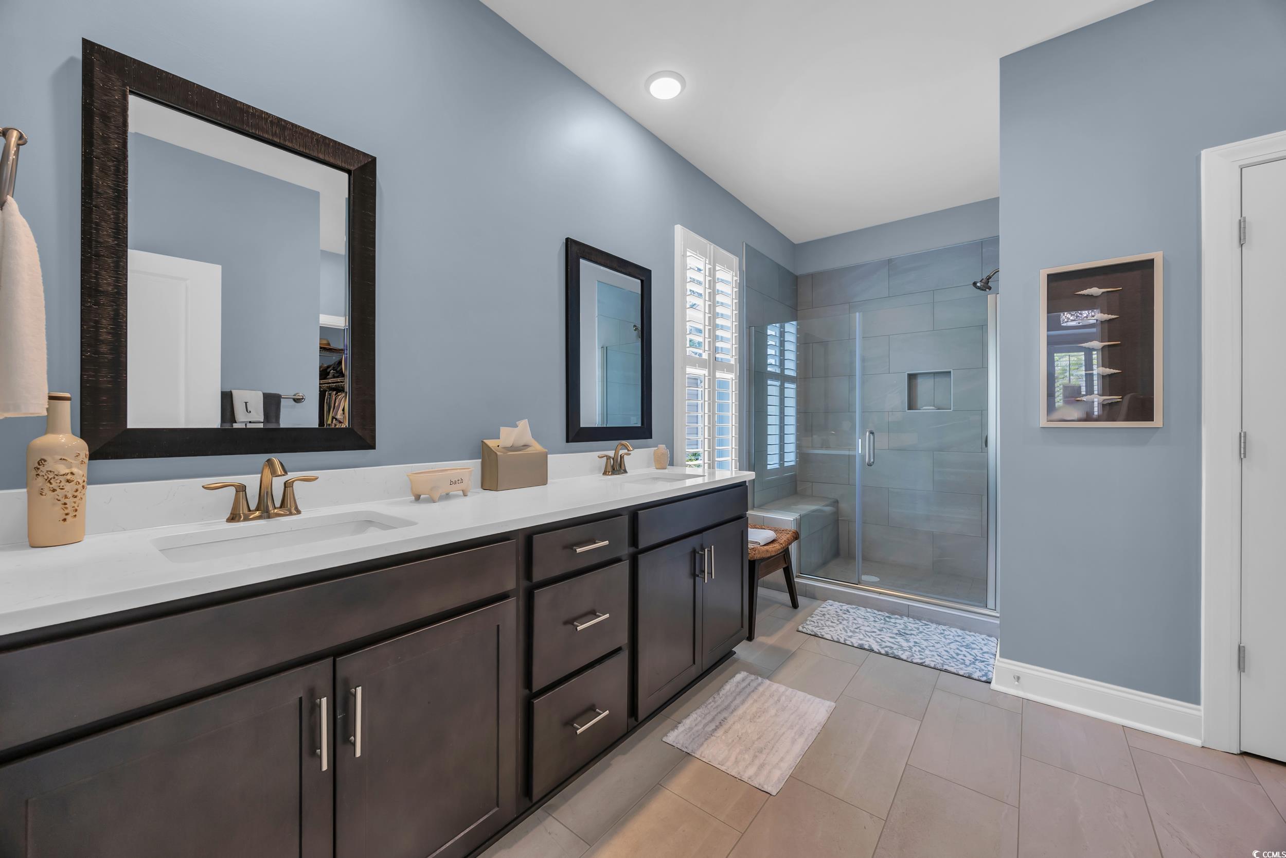 Full bath featuring a shower stall, double vanity, baseboards, and tile patterned flooring