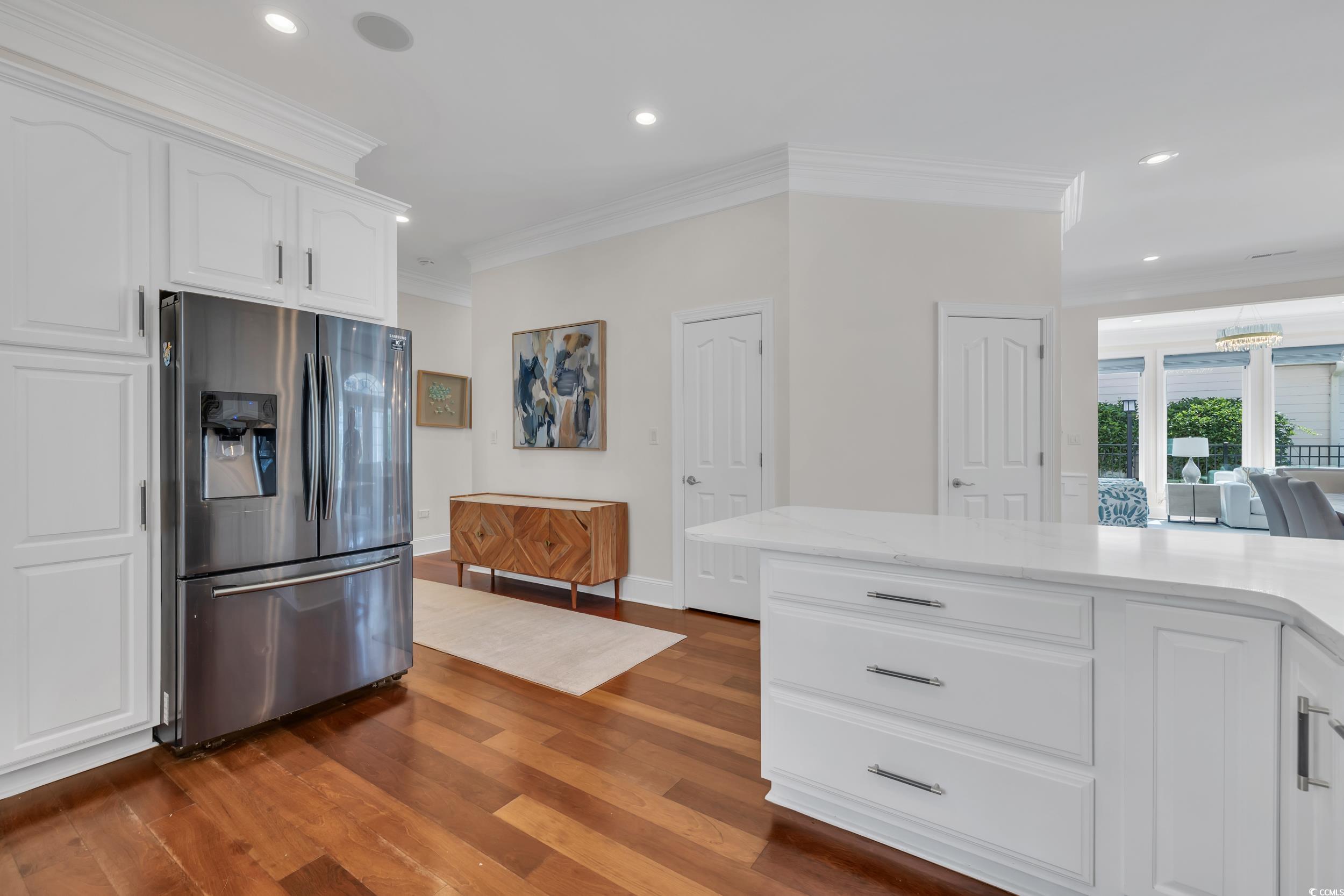 Kitchen featuring stainless steel refrigerator with ice dispenser, ornamental molding, dark wood-style flooring, white cabinetry, and recessed lighting
