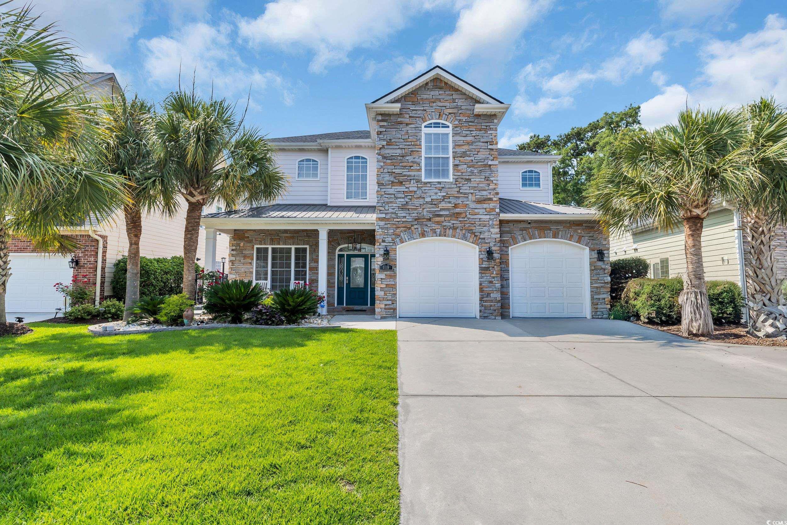 View of front of property with driveway, a front yard, an attached garage, a standing seam roof, and stone siding