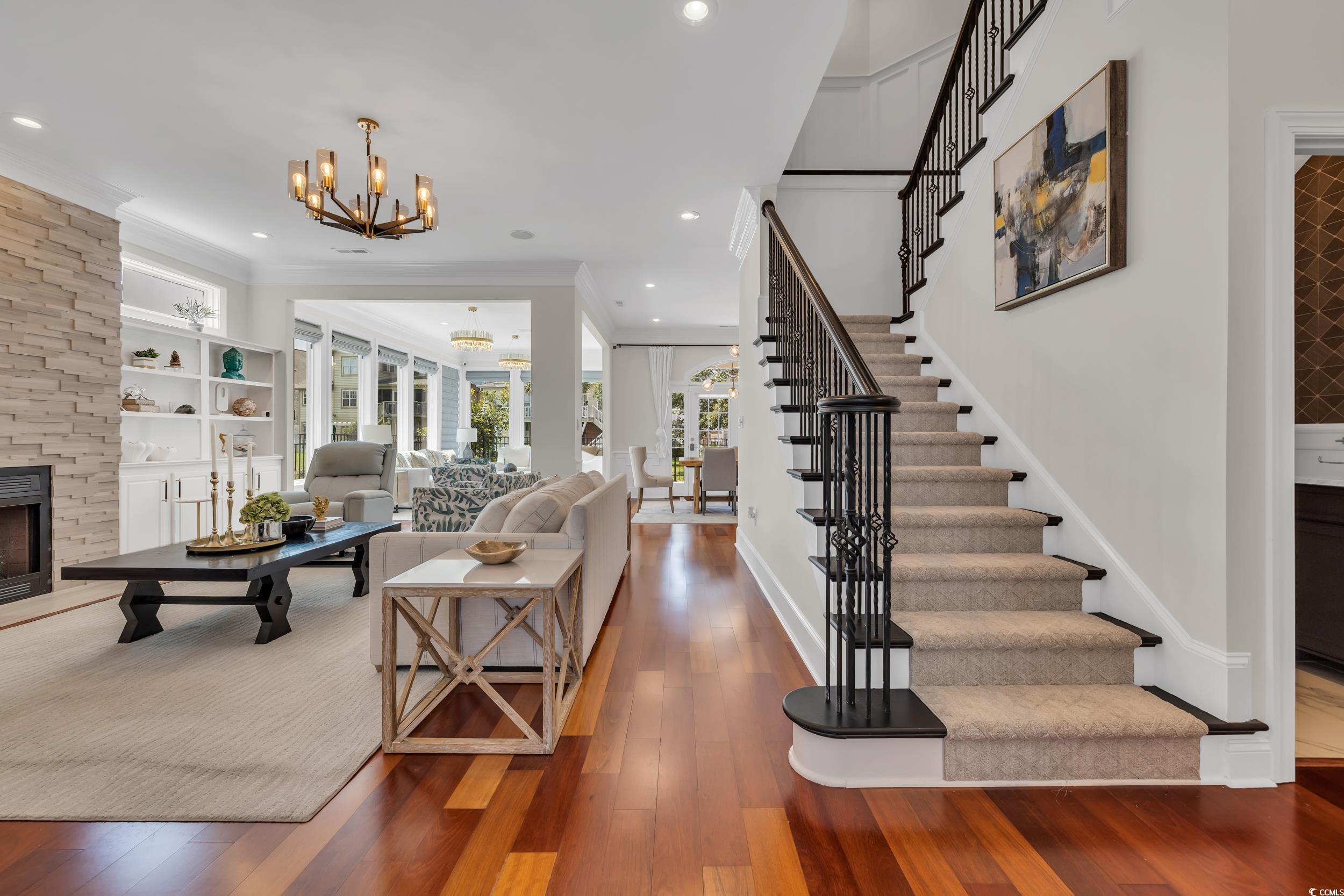 Living area with a chandelier, stairway, a fireplace, wood finished floors, and crown molding