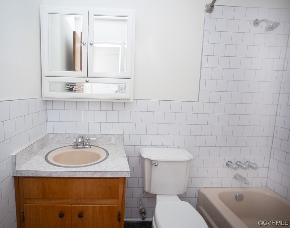 Full bathroom with tile walls, toilet, and tiled shower / bath