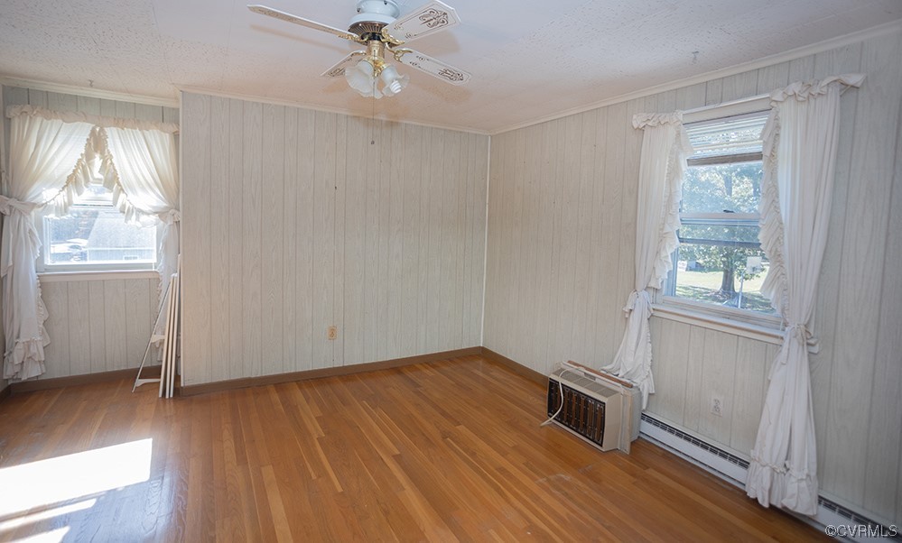 Spare room featuring light wood-type flooring, crown molding, ceiling fan, and baseboard heating