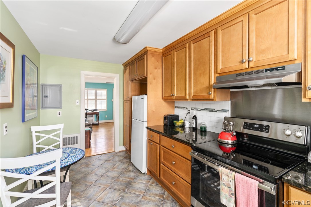 Kitchen with white fridge, hardwood / wood-style floors, electric stove, dark stone countertops, and backsplash