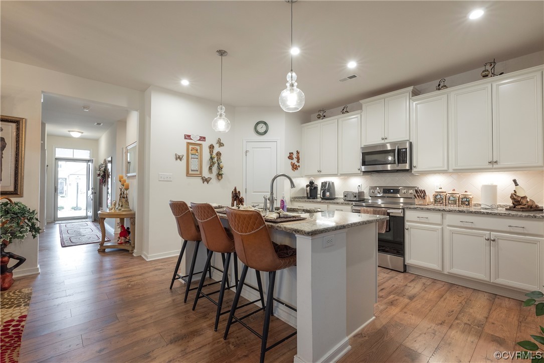 Kitchen with pendant lighting, hardwood / wood-style floors, white cabinetry, a center island with sink, and stainless steel appliances
