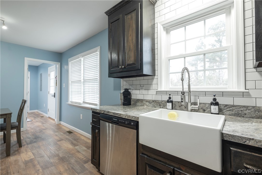 Kitchen featuring backsplash, dark brown cabinets, hardwood / wood-style floors, sink, and stainless steel dishwasher