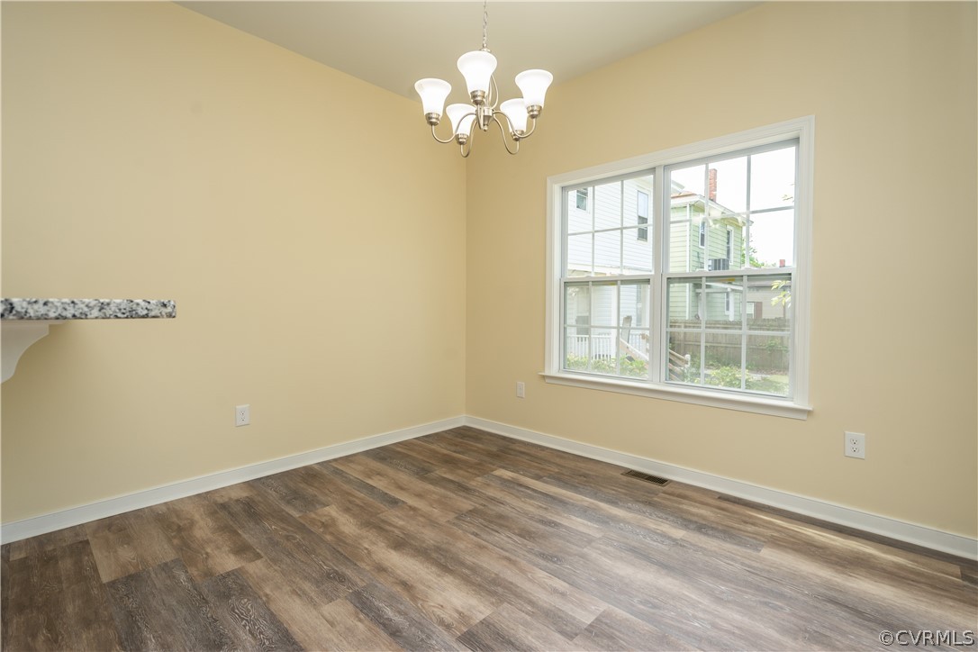 Spare room with dark hardwood / wood-style floors, a notable chandelier, and a healthy amount of sunlight