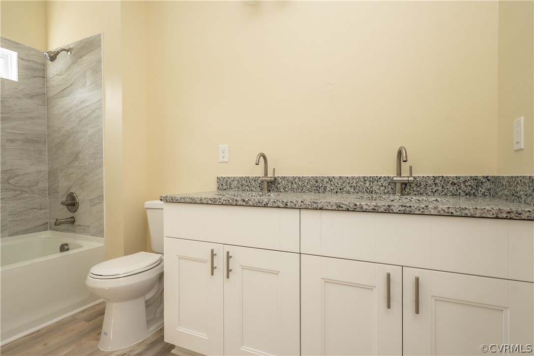 Full bathroom with toilet, hardwood / wood-style floors, tiled shower / bath combo, and vanity