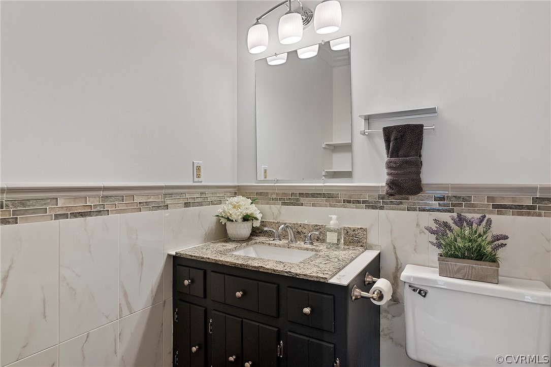 Bathroom featuring backsplash, toilet, oversized vanity, and tile walls