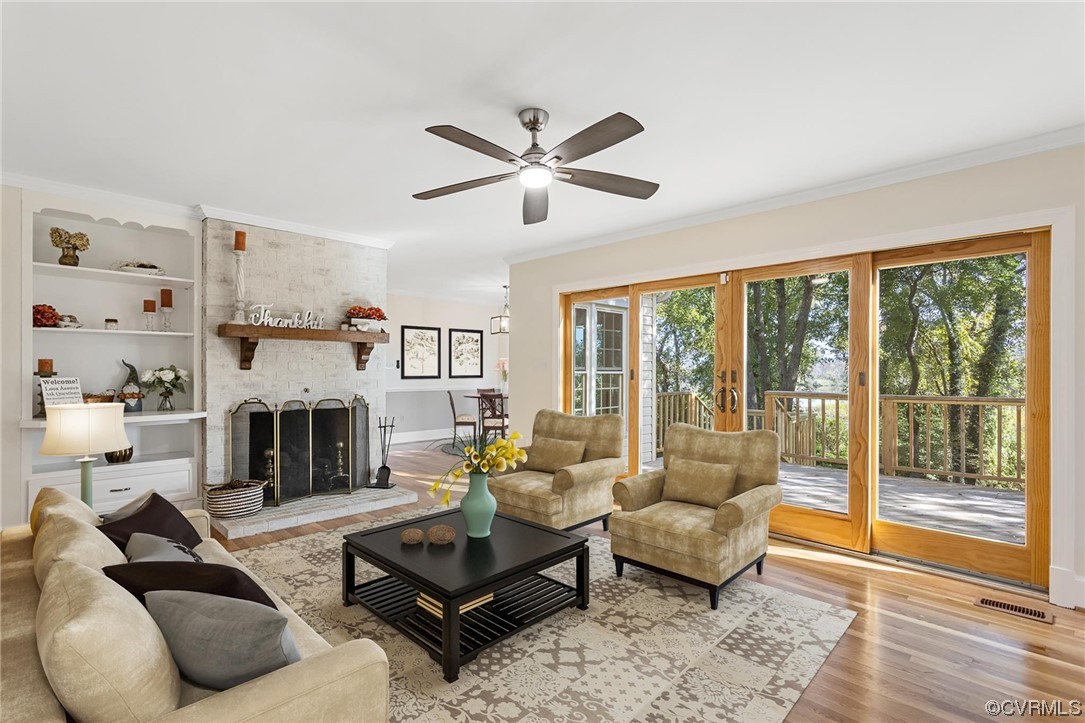 Hardwood floored living room with french doors, crown molding, a fireplace, and ceiling fan