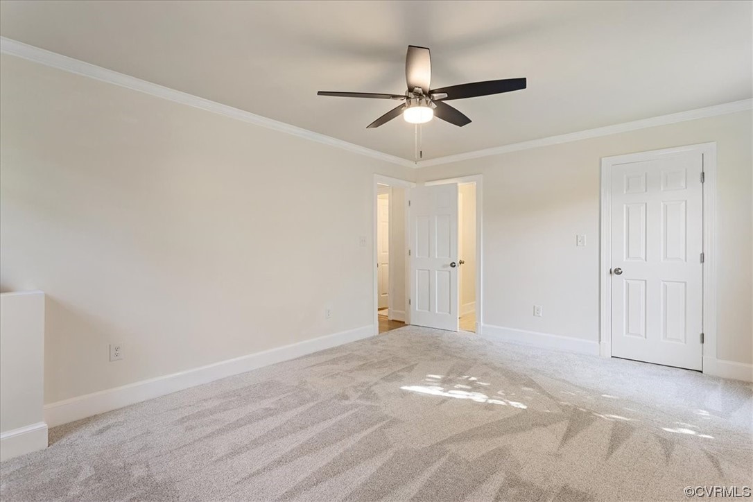 First Floor Primary Bedroom with light colored carpet, crown molding, and ceiling fan