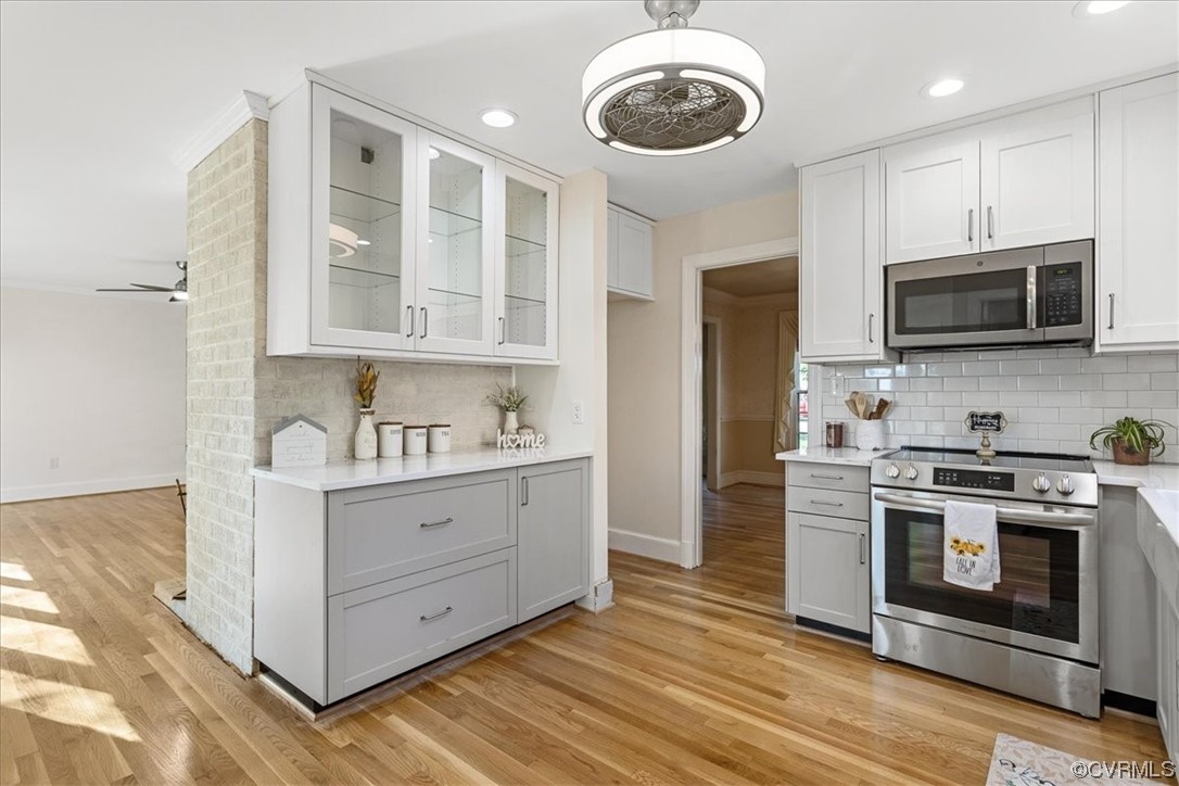 Kitchen with ceiling fan, light hardwood flooring, white cabinetry, tasteful backsplash, and appliances with stainless steel finishes and Quartz Countertops