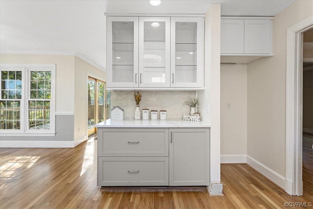 Kitchen with Quartz Countertops, tasteful backsplash, white cabinets, light hardwood flooring, and ornamental molding