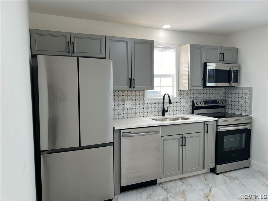 Kitchen with light tile floors, sink, stainless steel appliances, gray cabinets, and backsplash