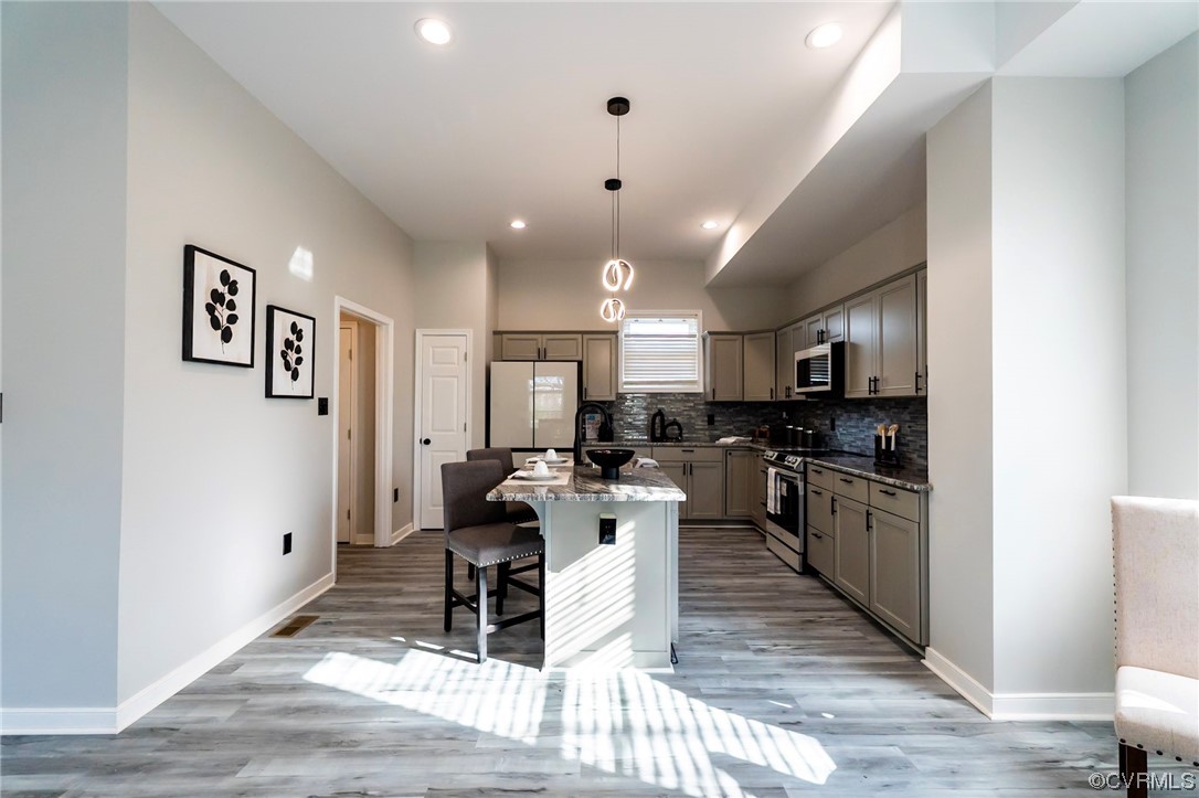 Kitchen featuring dark stone counters, a kitchen breakfast bar, pendant lighting, light hardwood / wood-style flooring, and stainless steel appliances