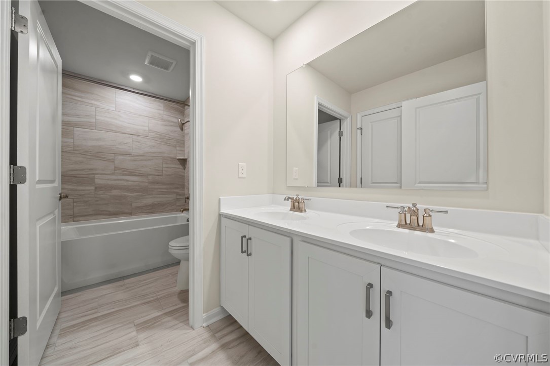 Full bathroom with tiled shower / bath, toilet, tile flooring, and dual vanity